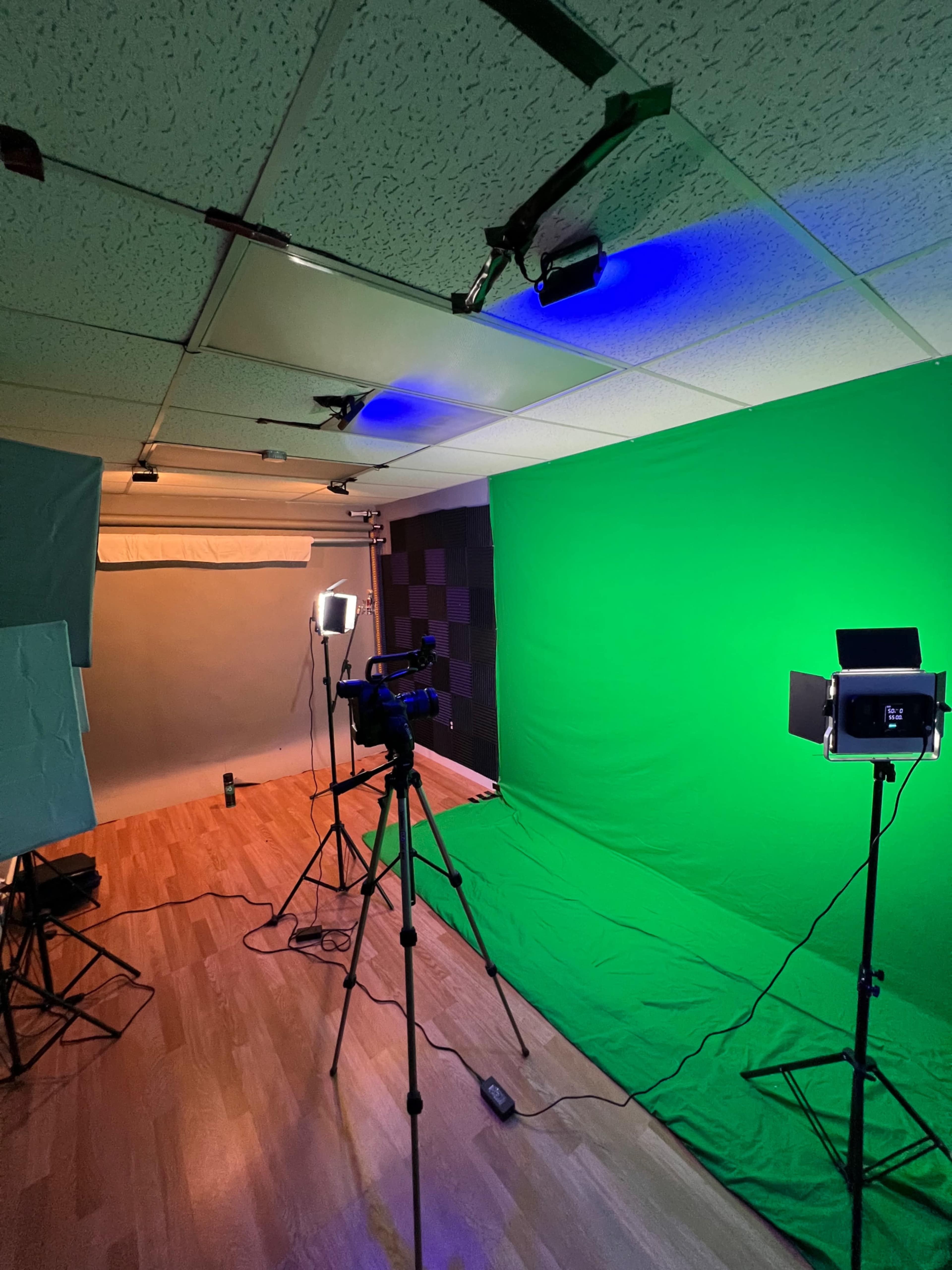 A video recording studio setup with a green screen, lighting equipment, and a camera on a tripod.