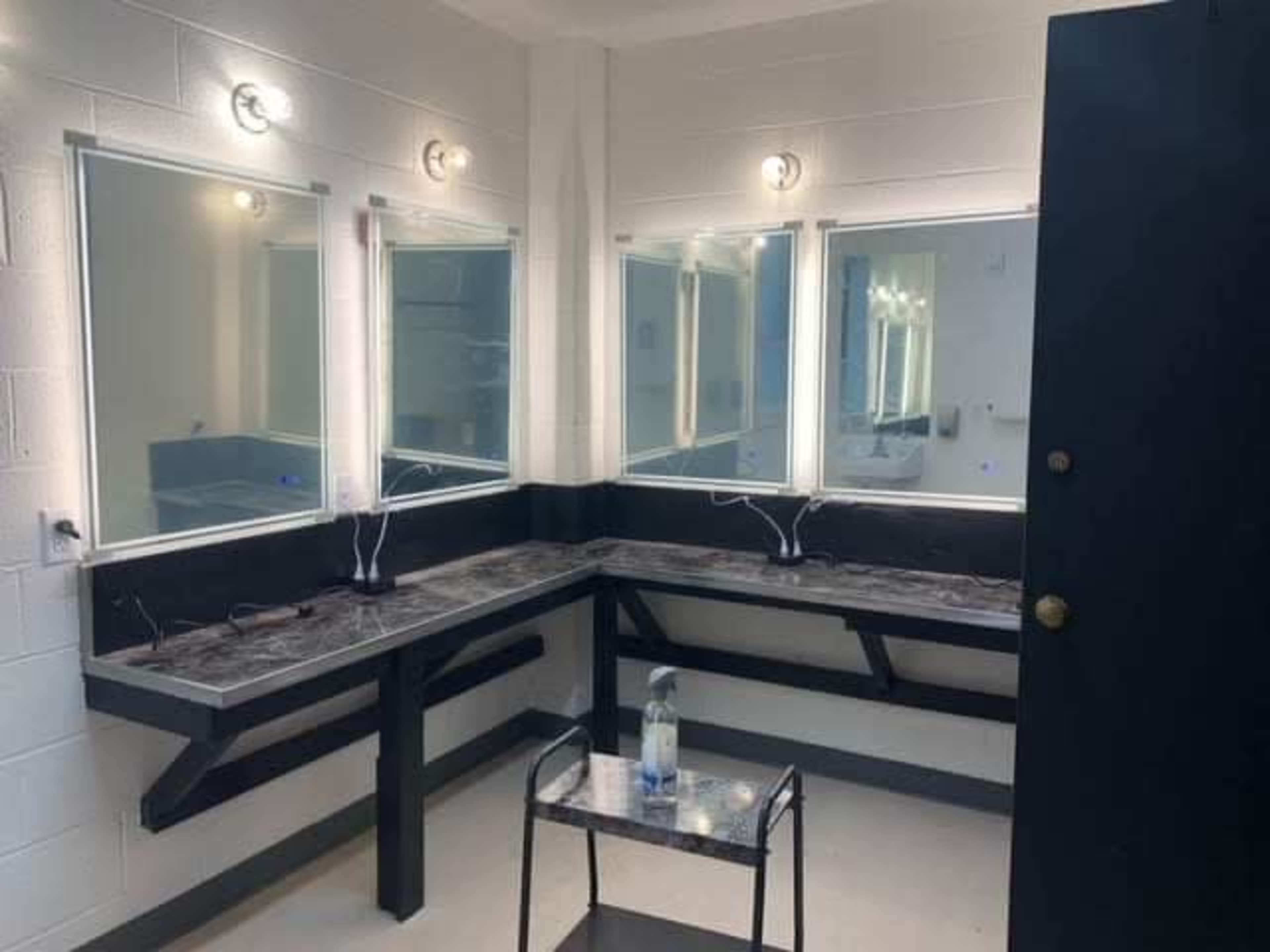 A well-lit dressing room with three mirrors, a black table, and a water bottle on a small table.