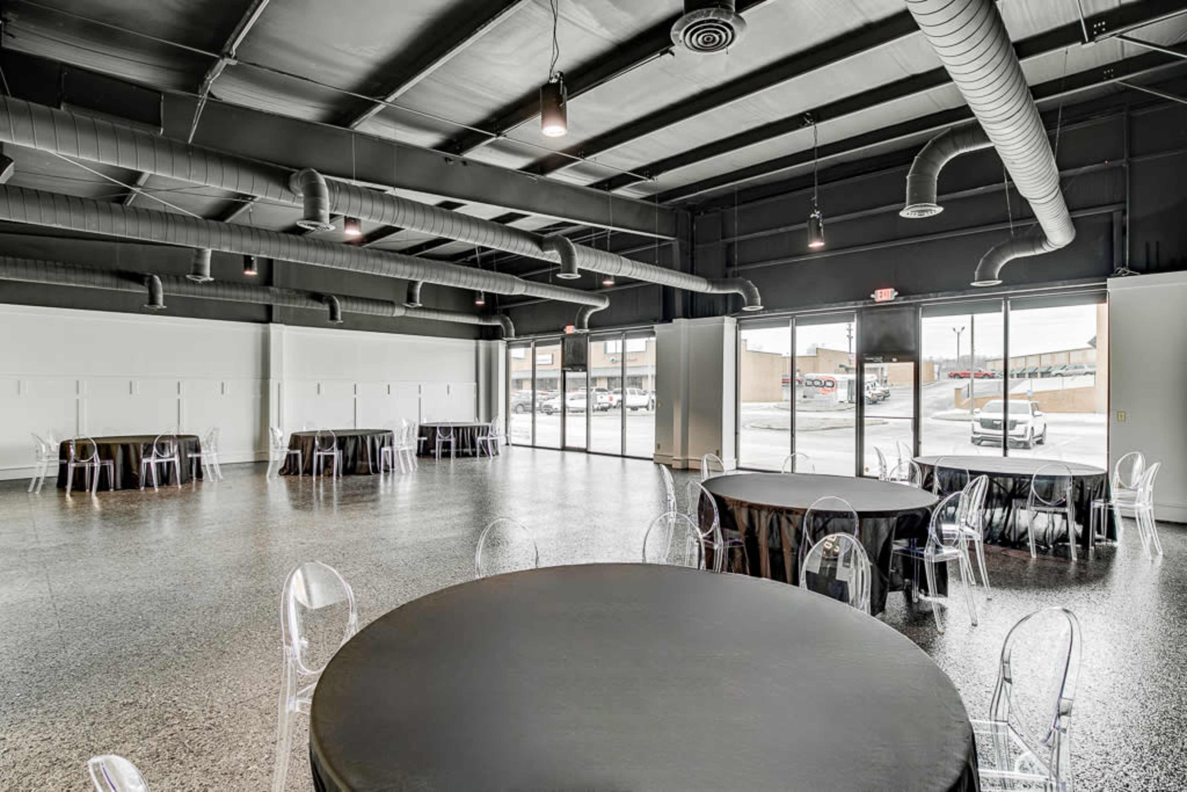 An empty event space with round tables covered in black tablecloths and large glass doors that open to an exterior view.