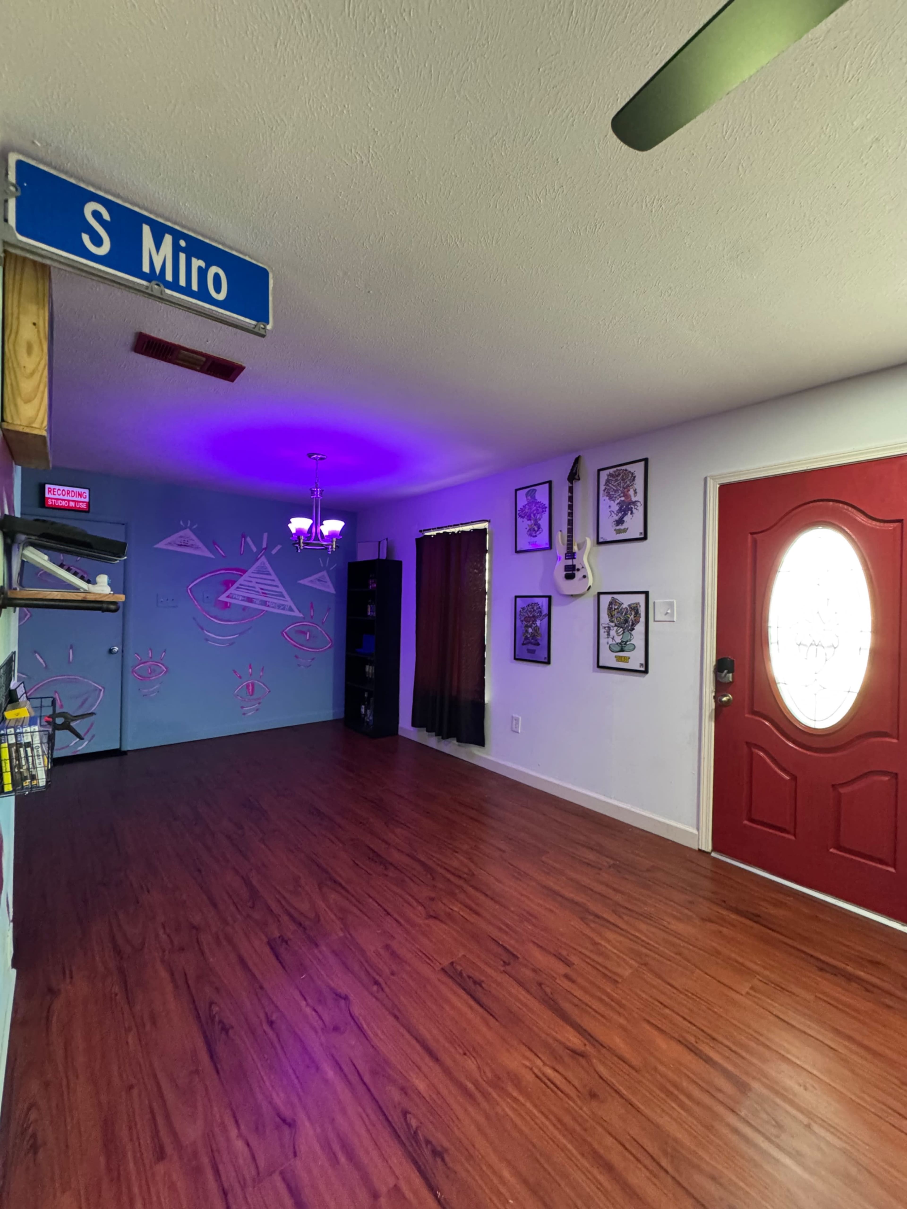 The room features a hardwood floor, purple accent lighting, a red door, and artwork on the walls, with a sign labeled "S Miro" above.