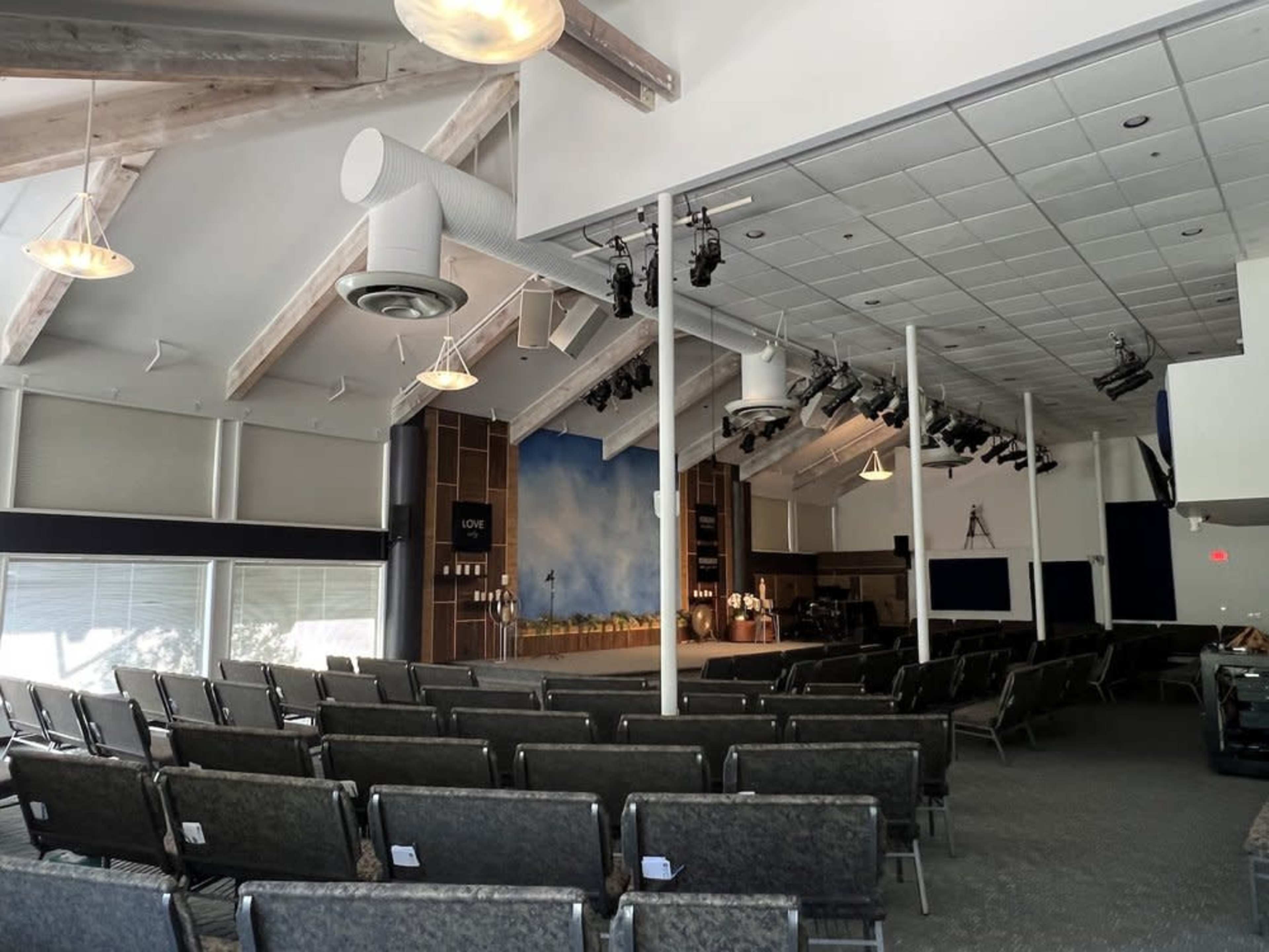 A modern church interior with rows of empty chairs facing a stage illuminated by overhead lighting.