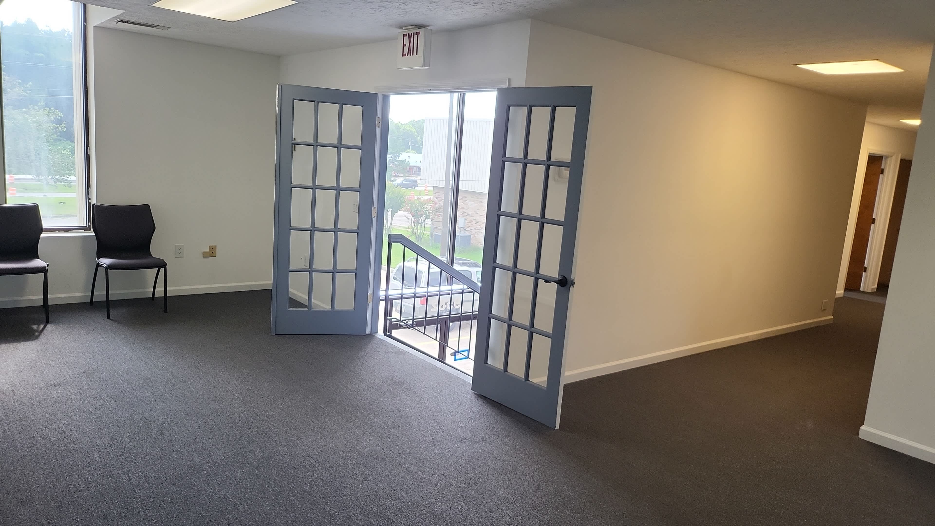 The image shows an empty office space featuring two open French doors leading to a staircase and two chairs positioned nearby.