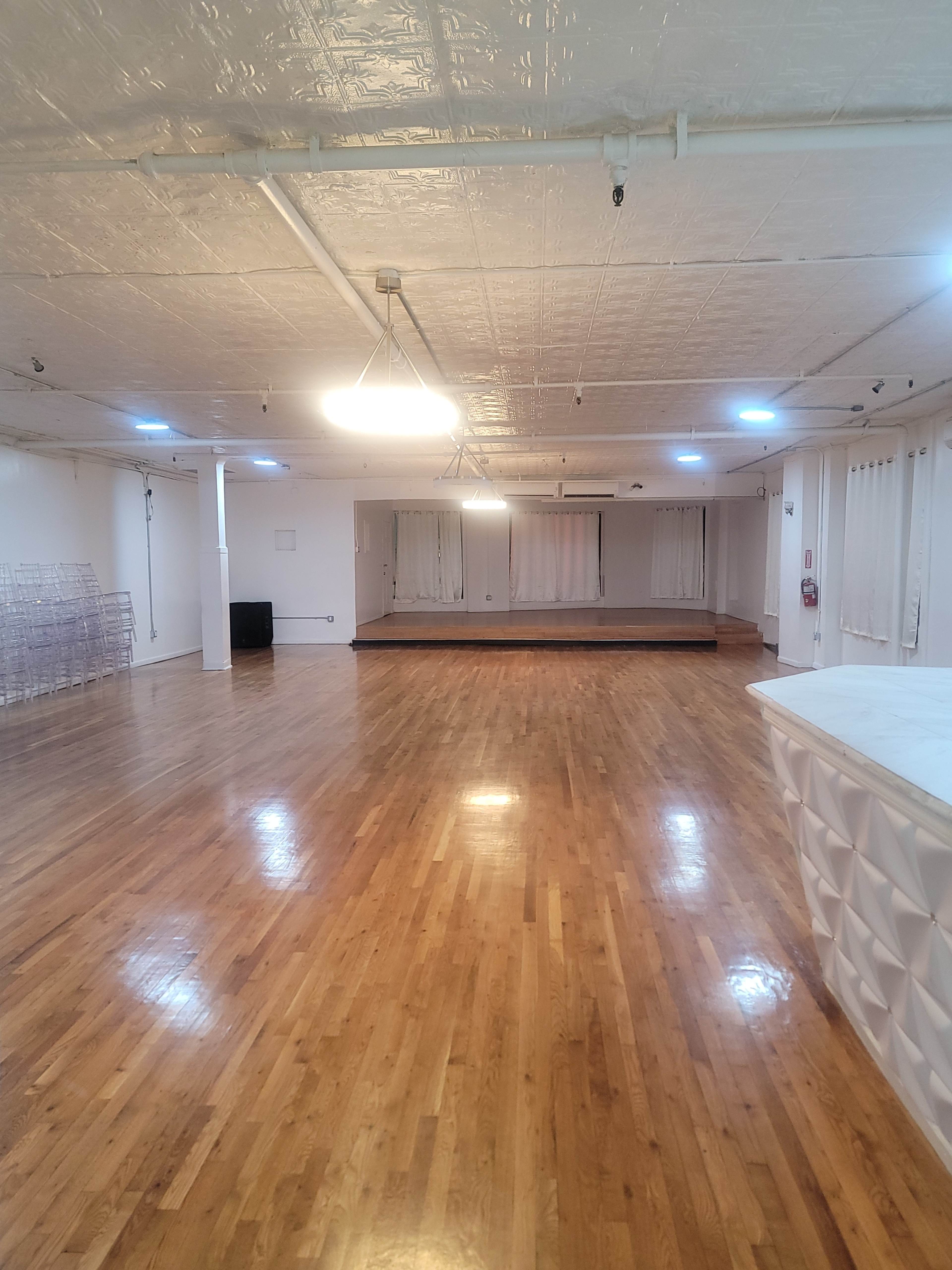 A spacious room with hardwood flooring, bright overhead lighting, and a raised platform at one end.