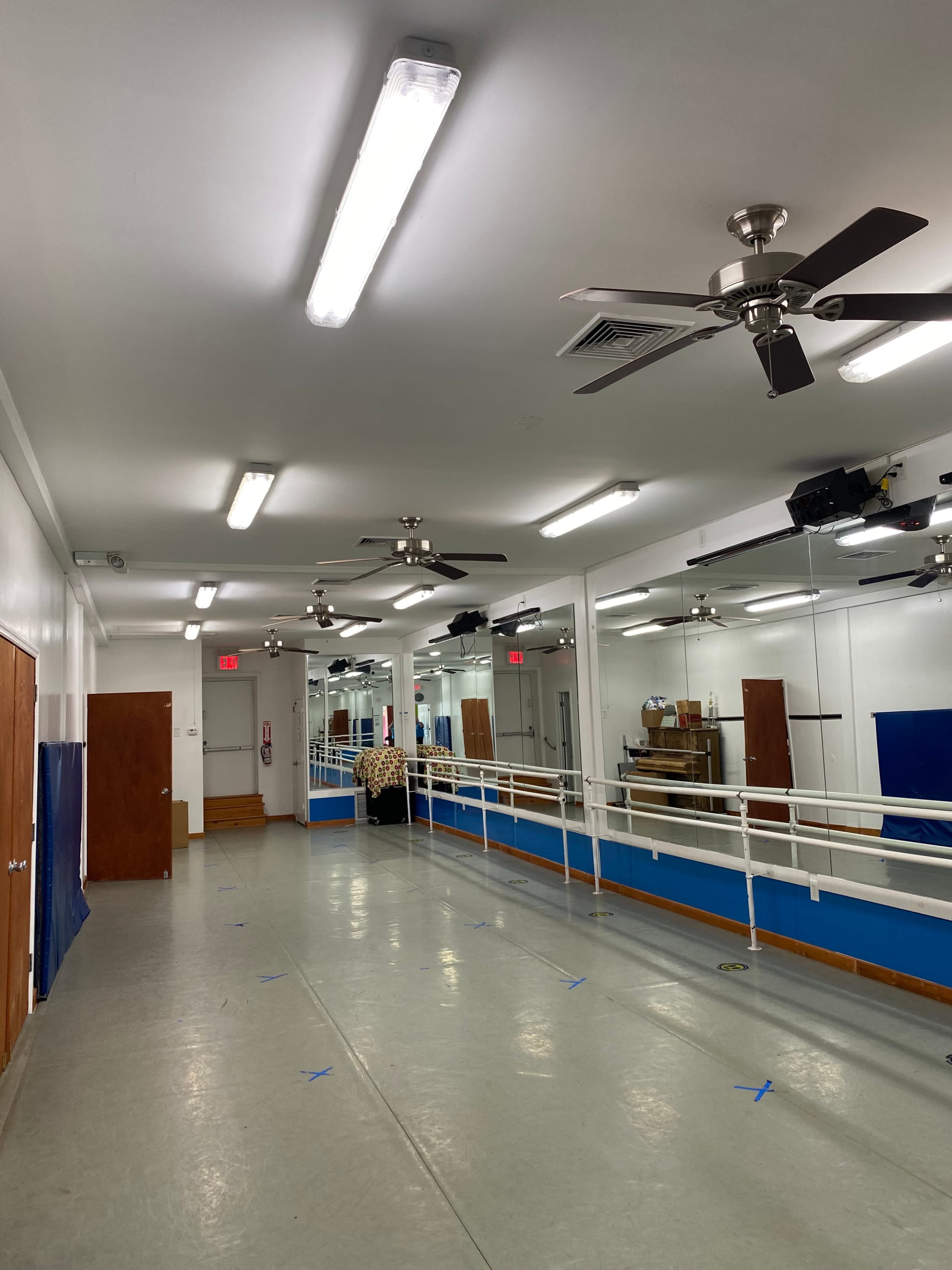 A well-lit dance studio with mirrors along one wall, wooden doors, and a ballet barre on the opposite side.