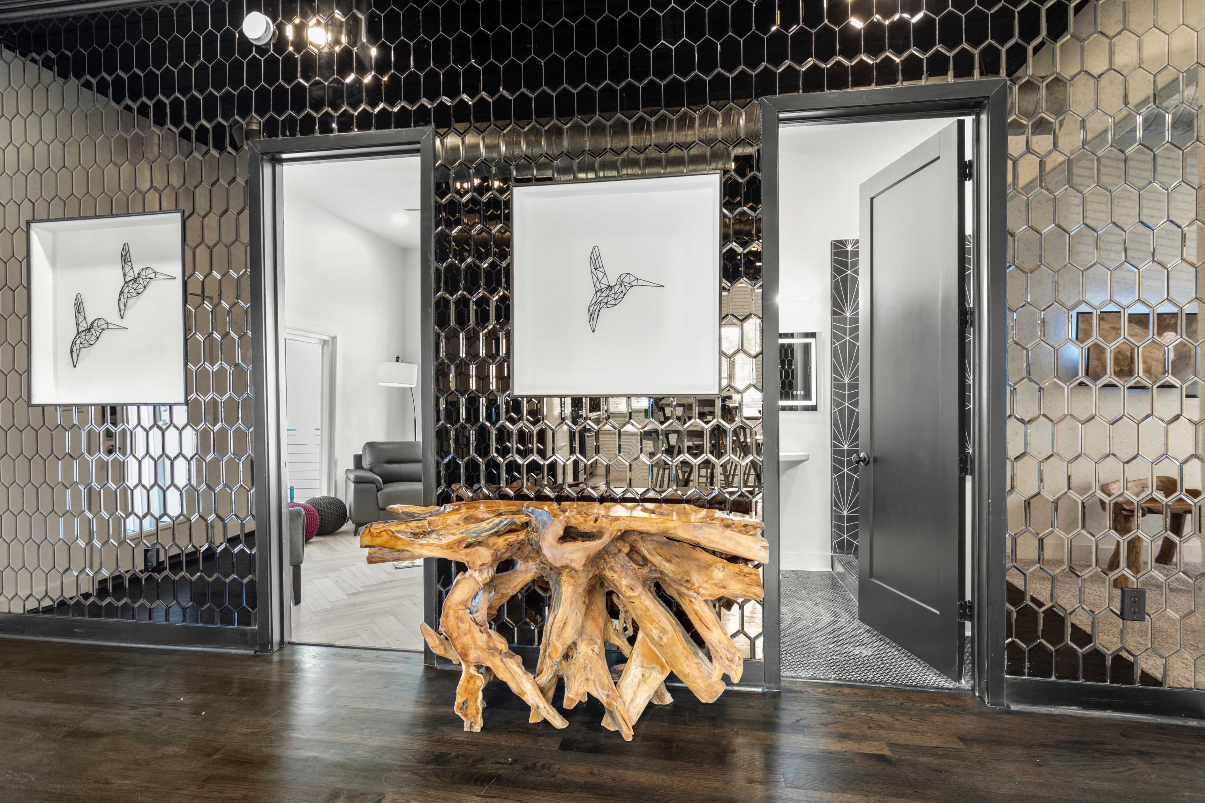 An entrance area featuring a unique wooden console table, two framed artworks of birds, and large mirrored walls reflecting the space.