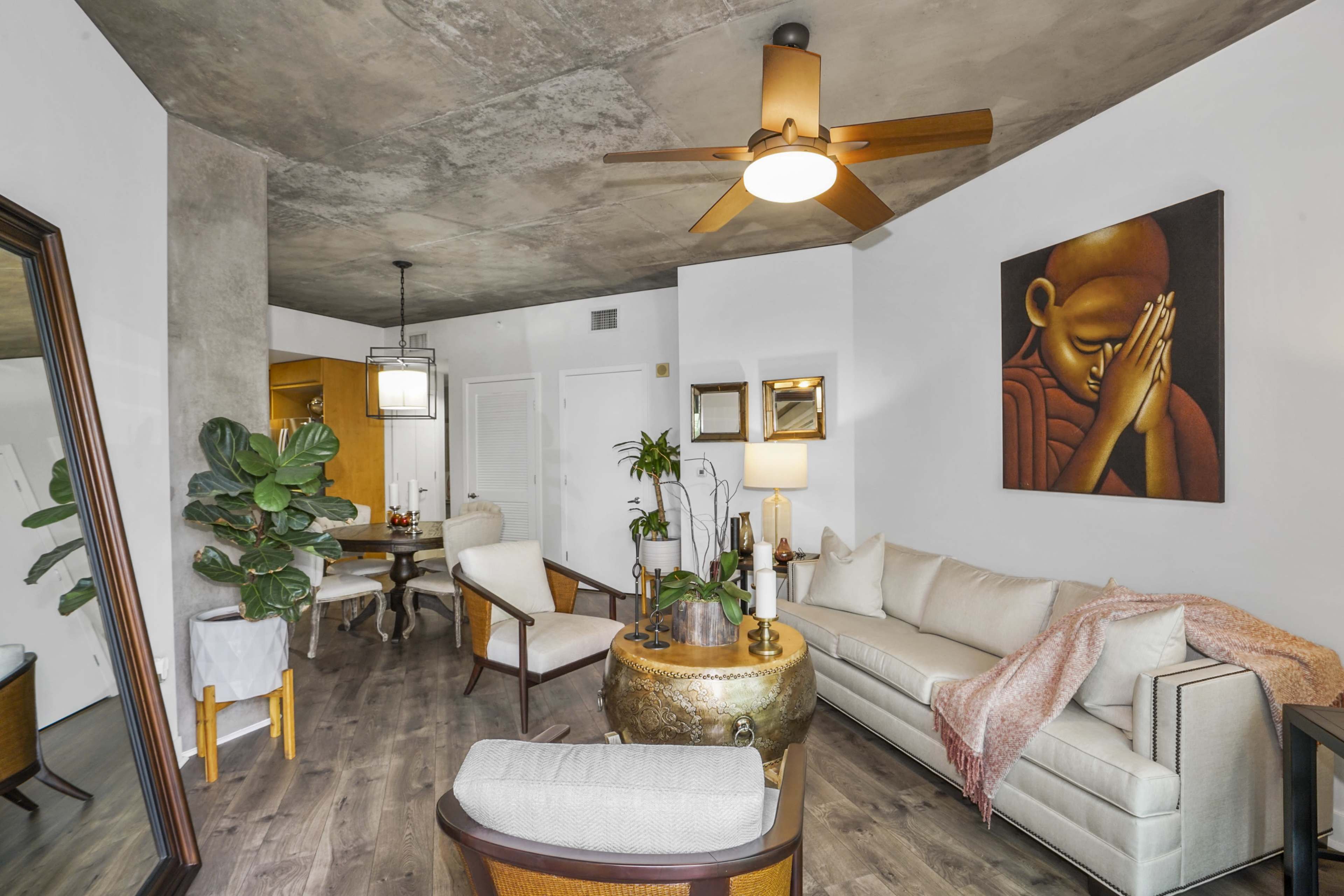 A modern living room with a concrete ceiling, a beige sofa, a round wooden coffee table, and a large wall painting of a praying figure.