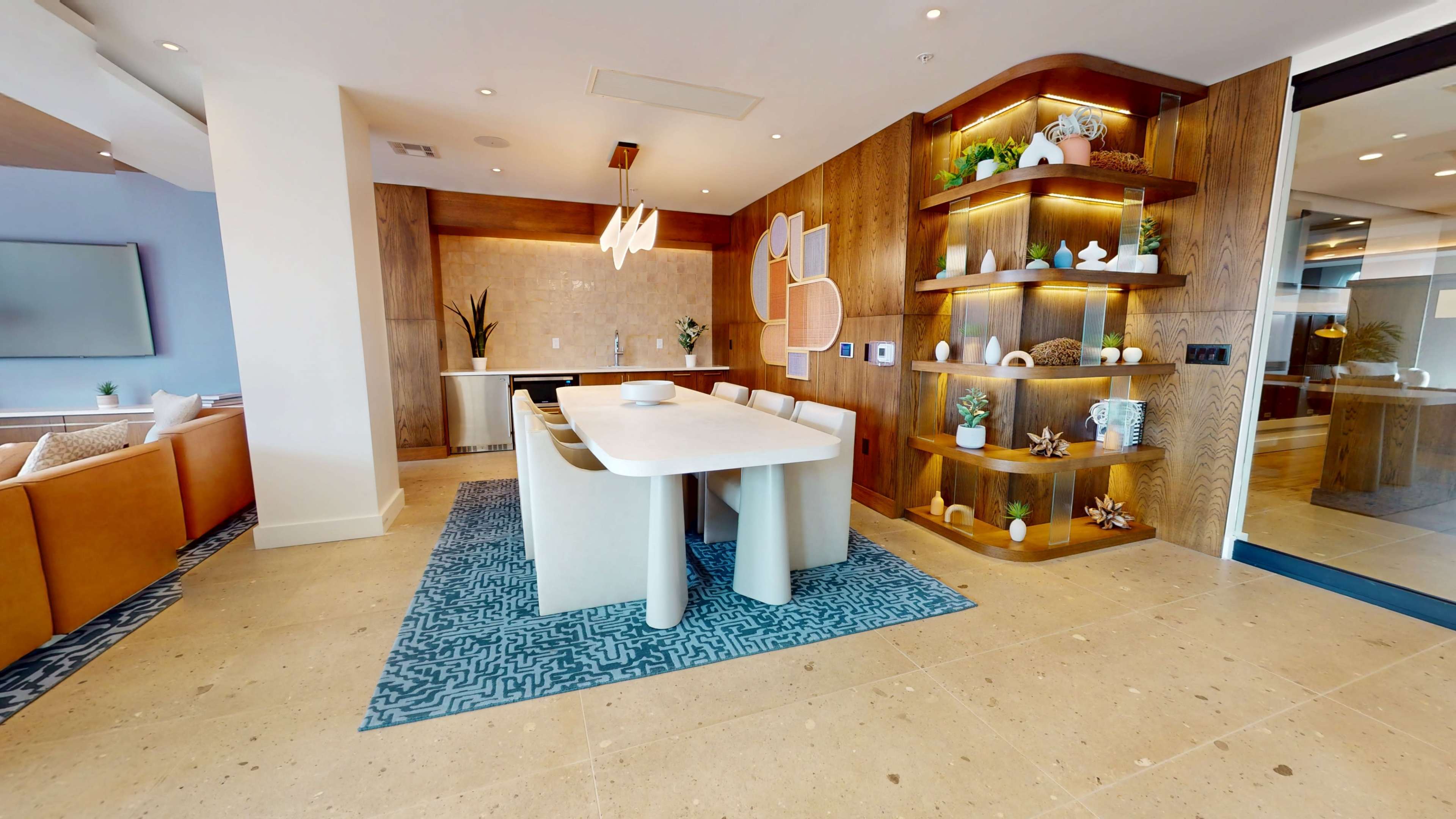The image shows a modern dining area featuring a white table surrounded by beige chairs, with a decorative shelving unit against the wall and a neutral-toned rug.