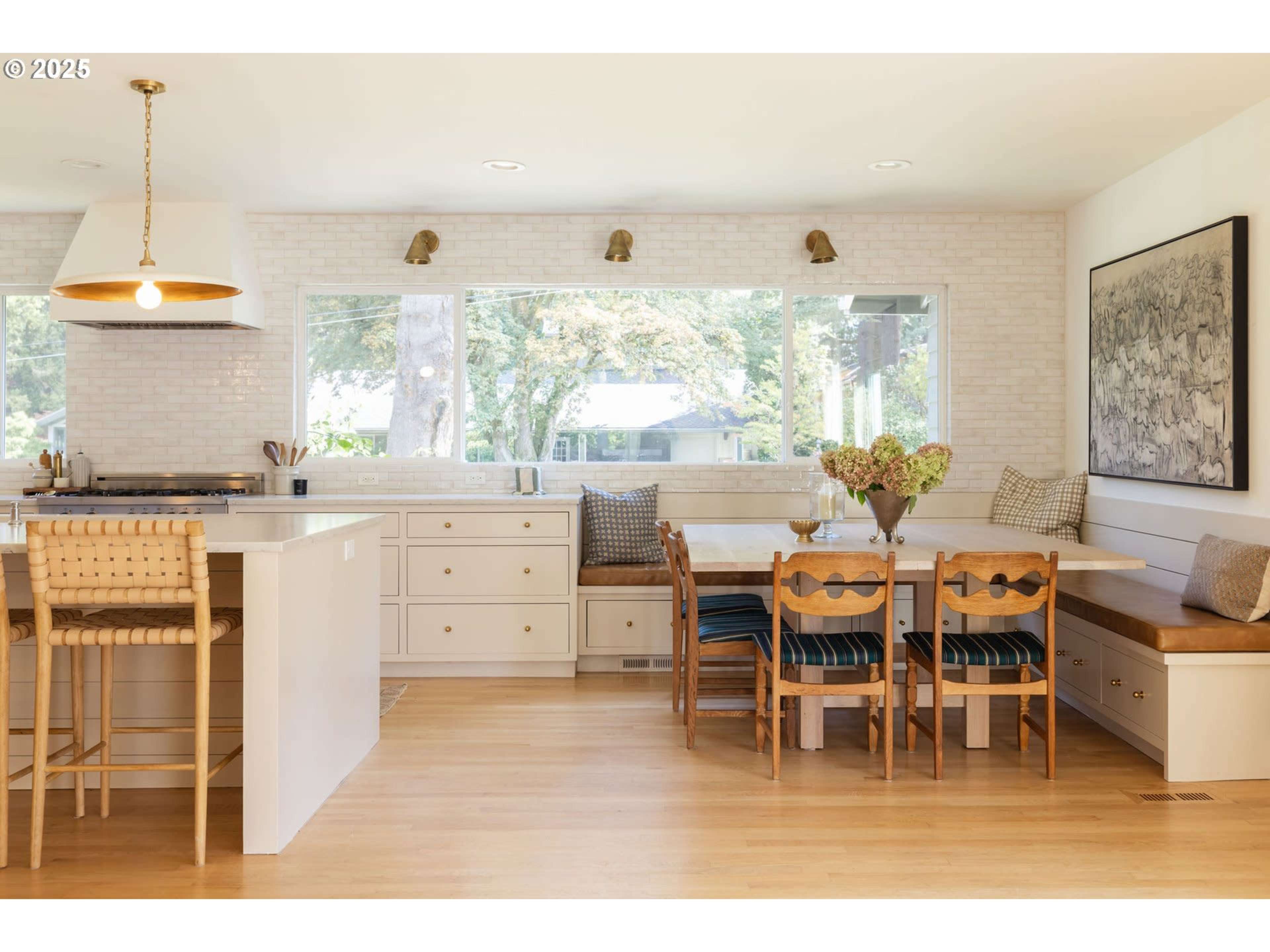 The kitchen features a modern design with a central island, dining area, and large windows overlooking a garden.