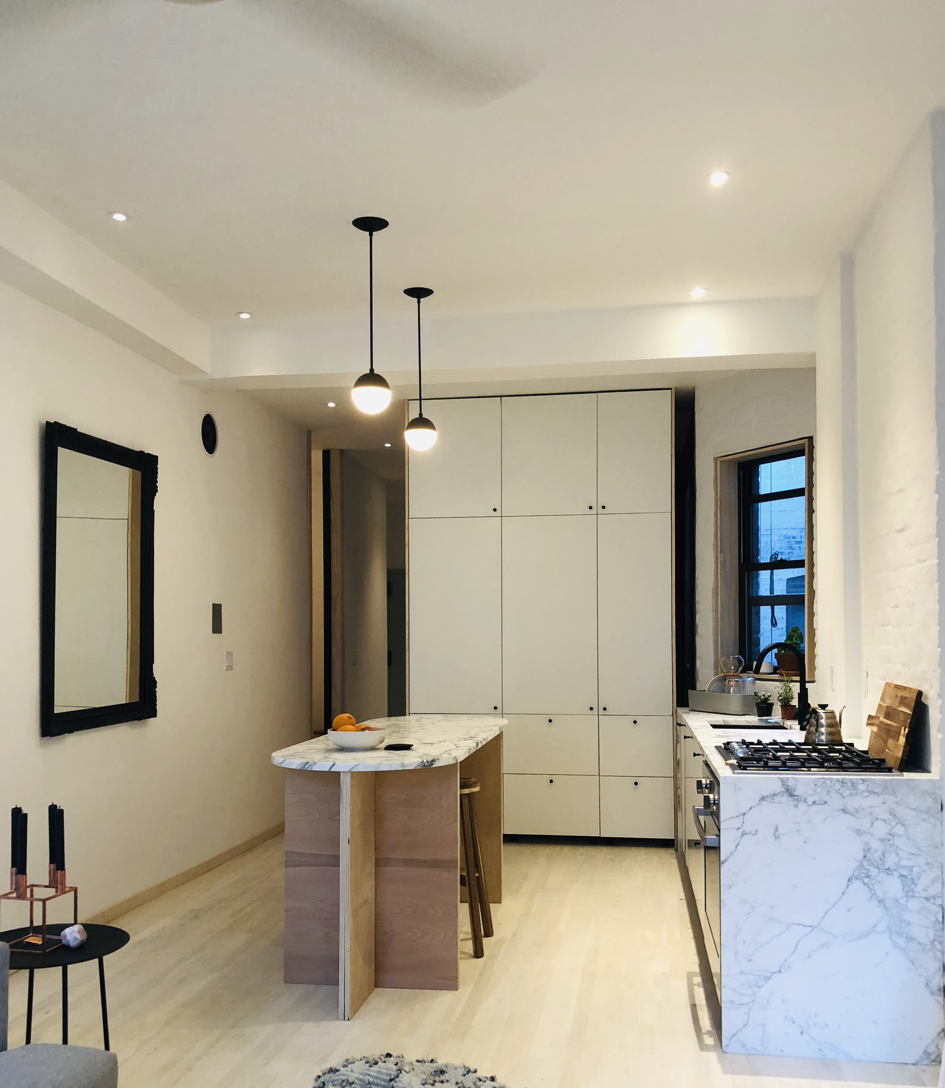 The image shows a modern kitchen featuring an island with a marble countertop, light-colored cabinetry, and sleek pendant lights.