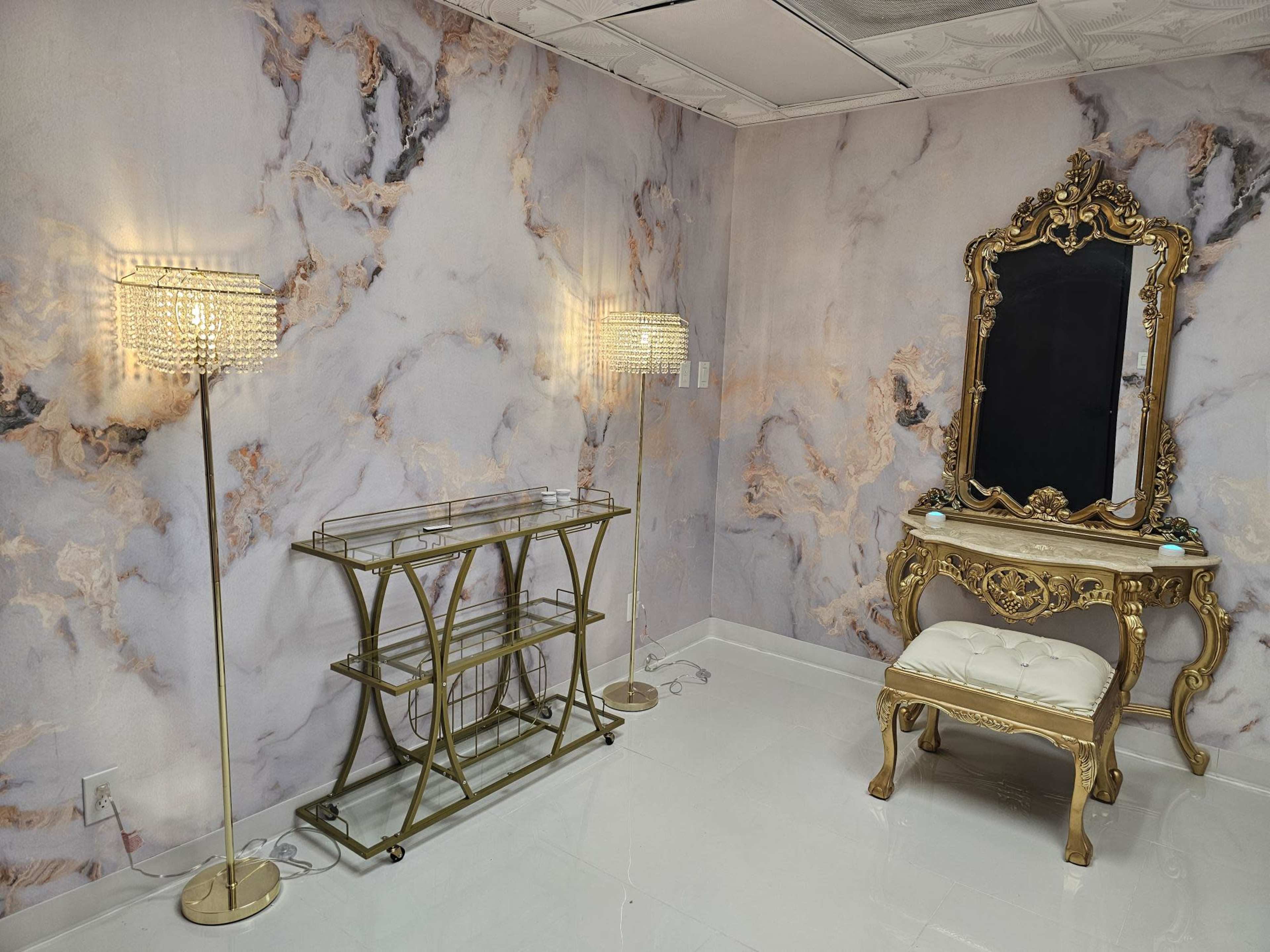 A room with marble-patterned walls, a gold-framed mirror, a decorative chair, and two floor lamps.