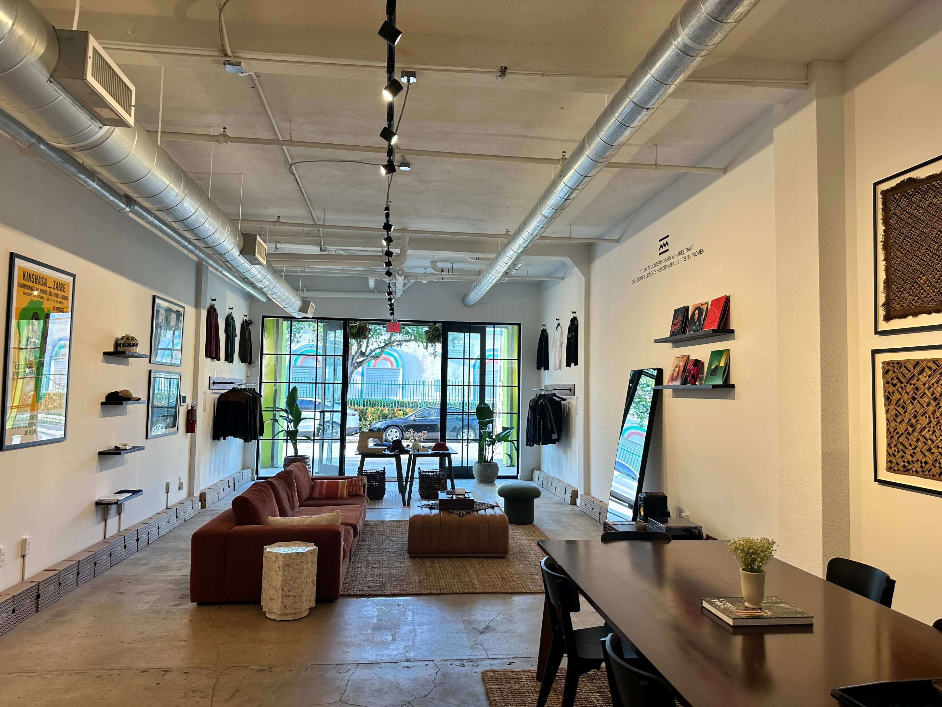 The image shows a modern retail space with a seating area, clothing display on the walls, and a large window that lets in natural light.