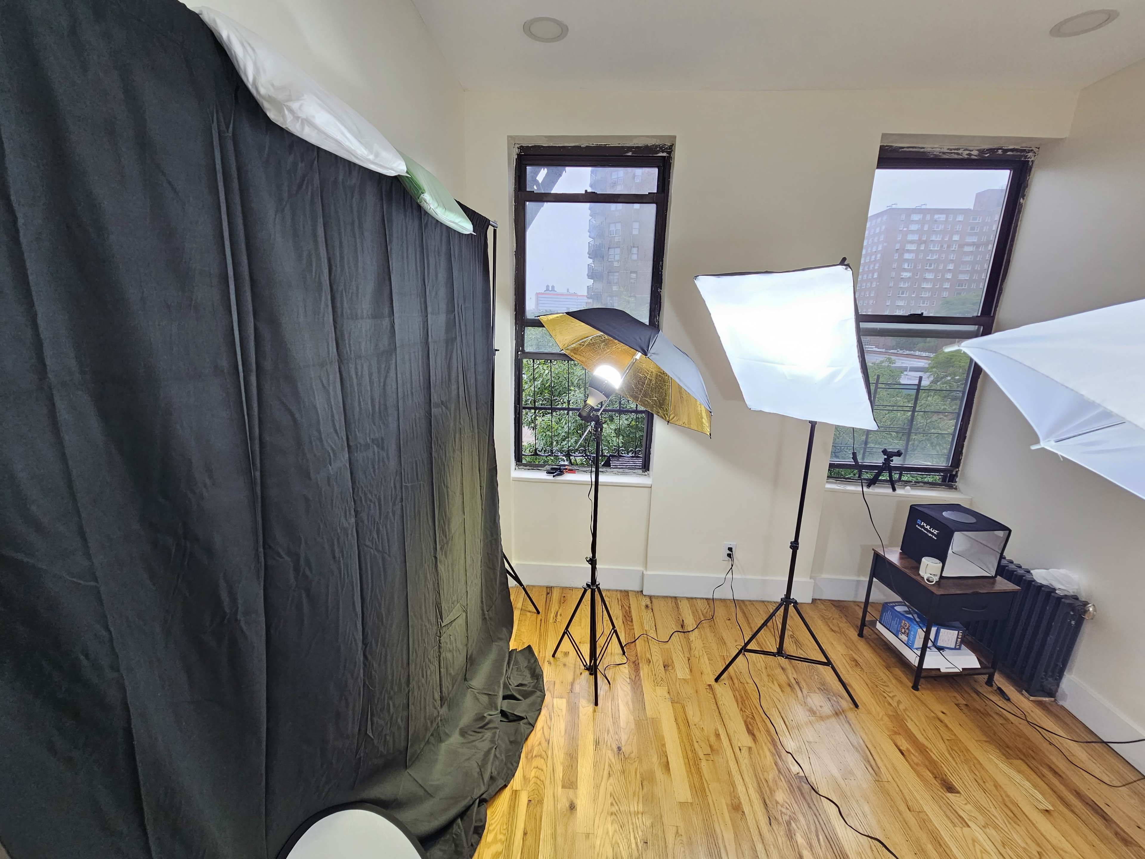 A well-lit room with a black backdrop, three light stands, and a shelf containing a box, all situated near windows.