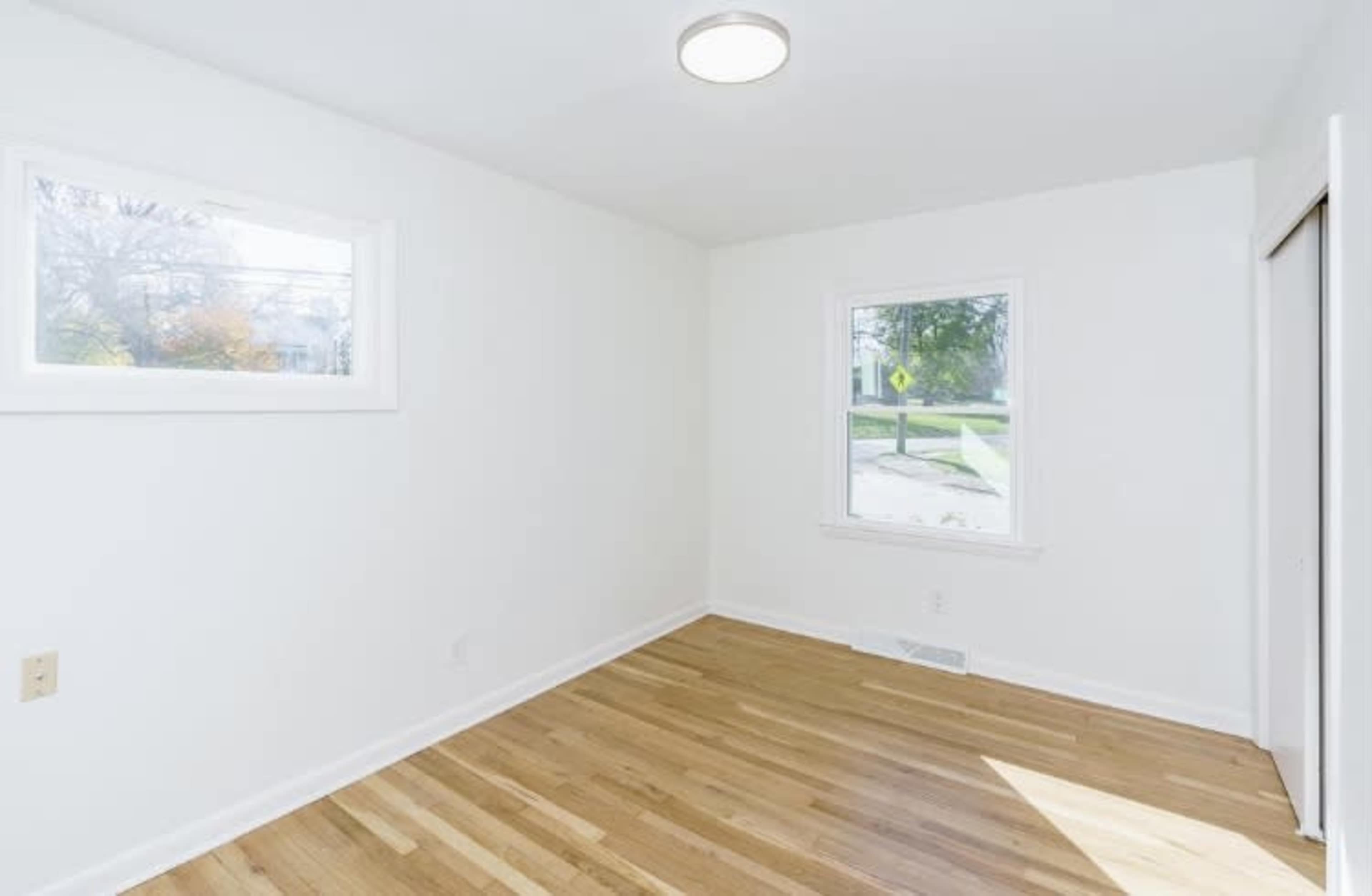 A small, empty room with hardwood floors and two windows.