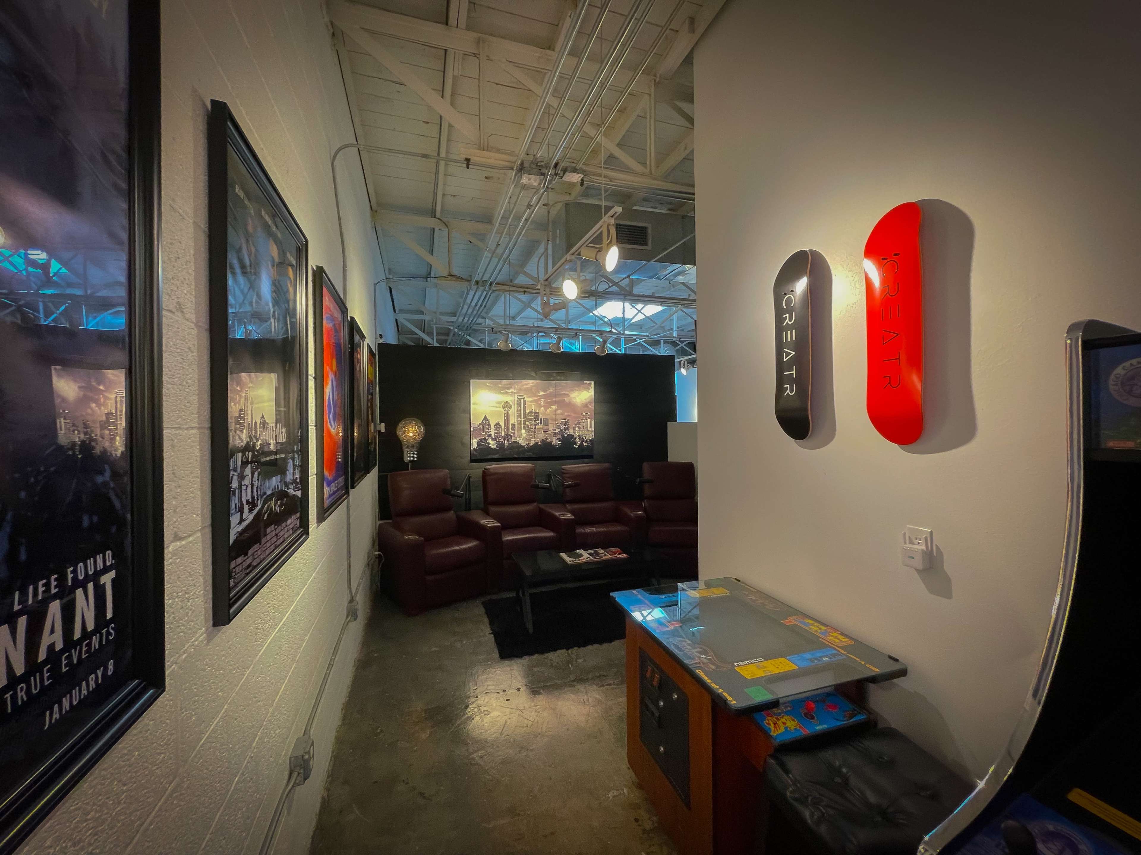 A modern lounge area with a red and black skateboard mounted on the wall, surrounded by leather couches and framed posters.