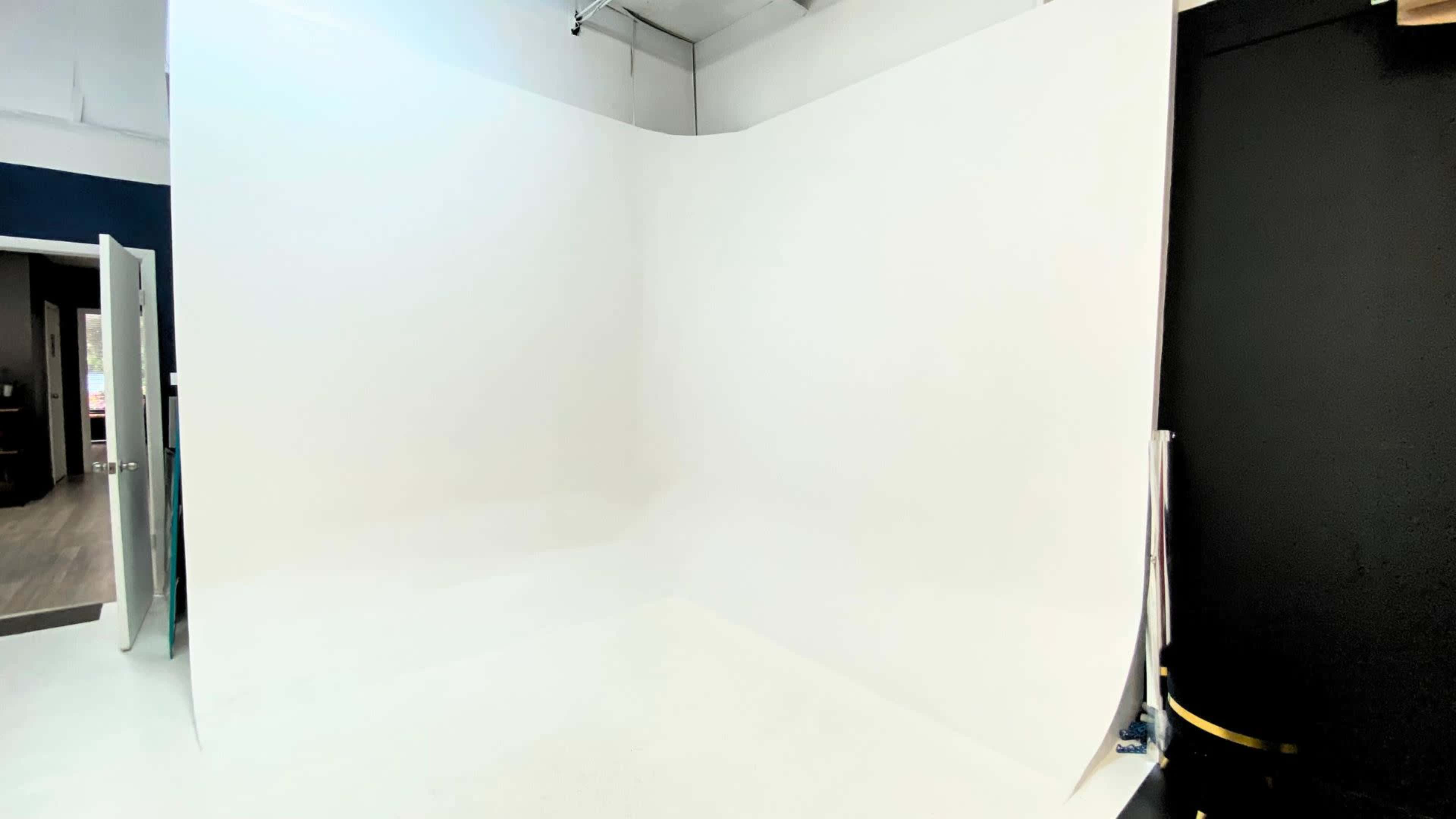 The image shows a clean, white studio space with a seamless backdrop and an open doorway.