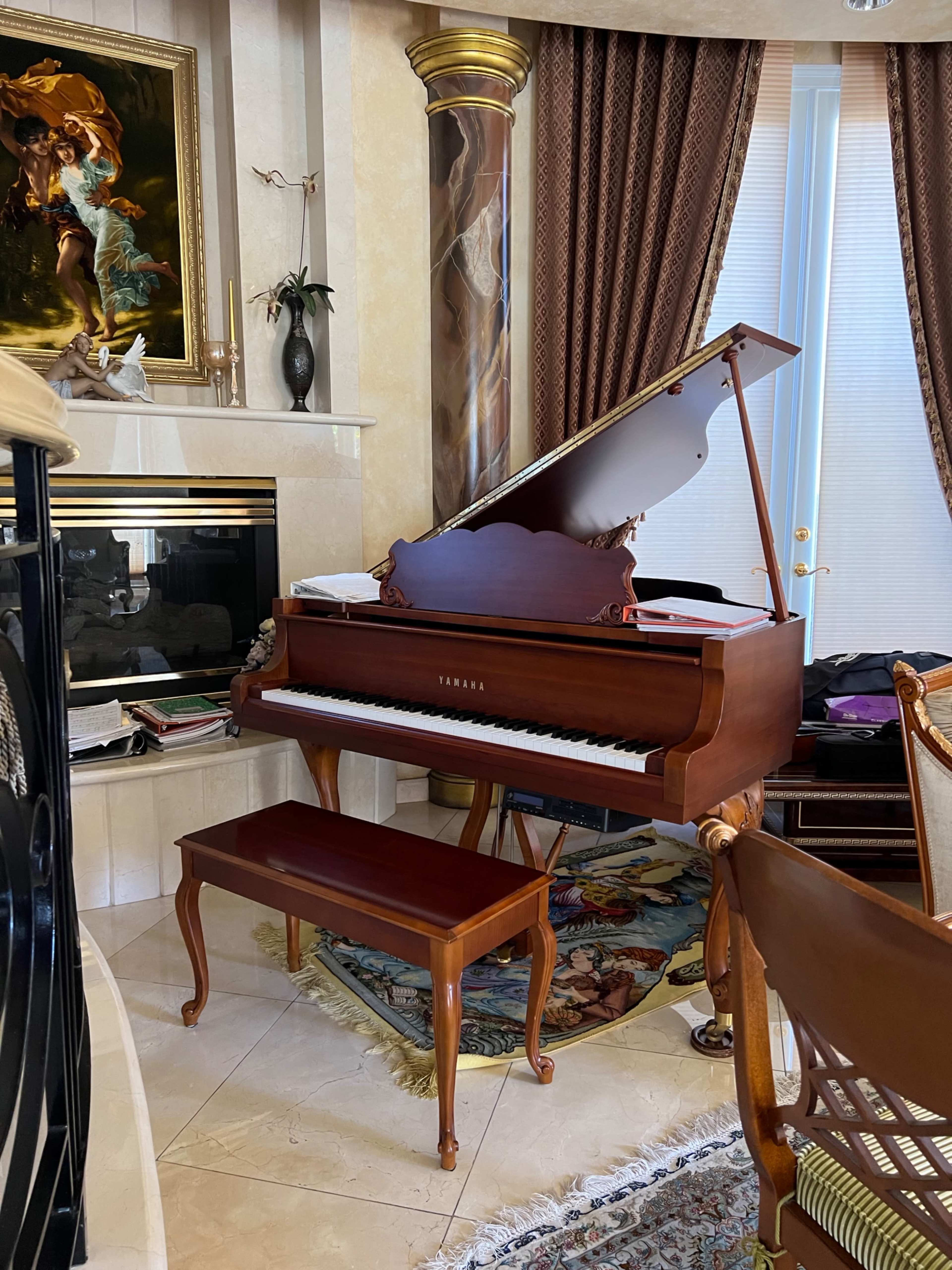 A grand piano with a matching bench sits beside a fireplace in a room adorned with ornate decor and furnishings.