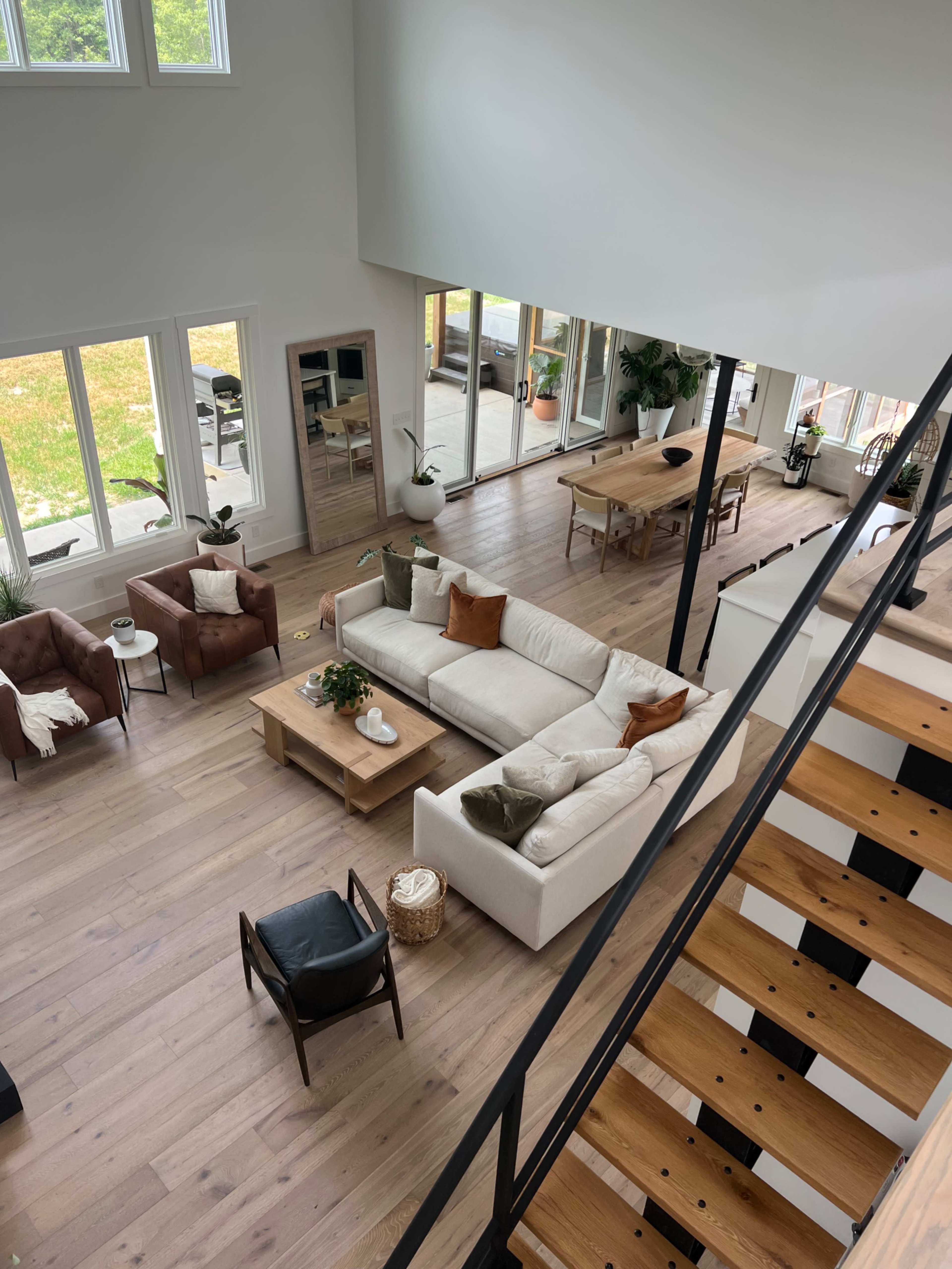 A spacious living area features a sectional sofa, wooden furniture, and large windows overlooking a yard.