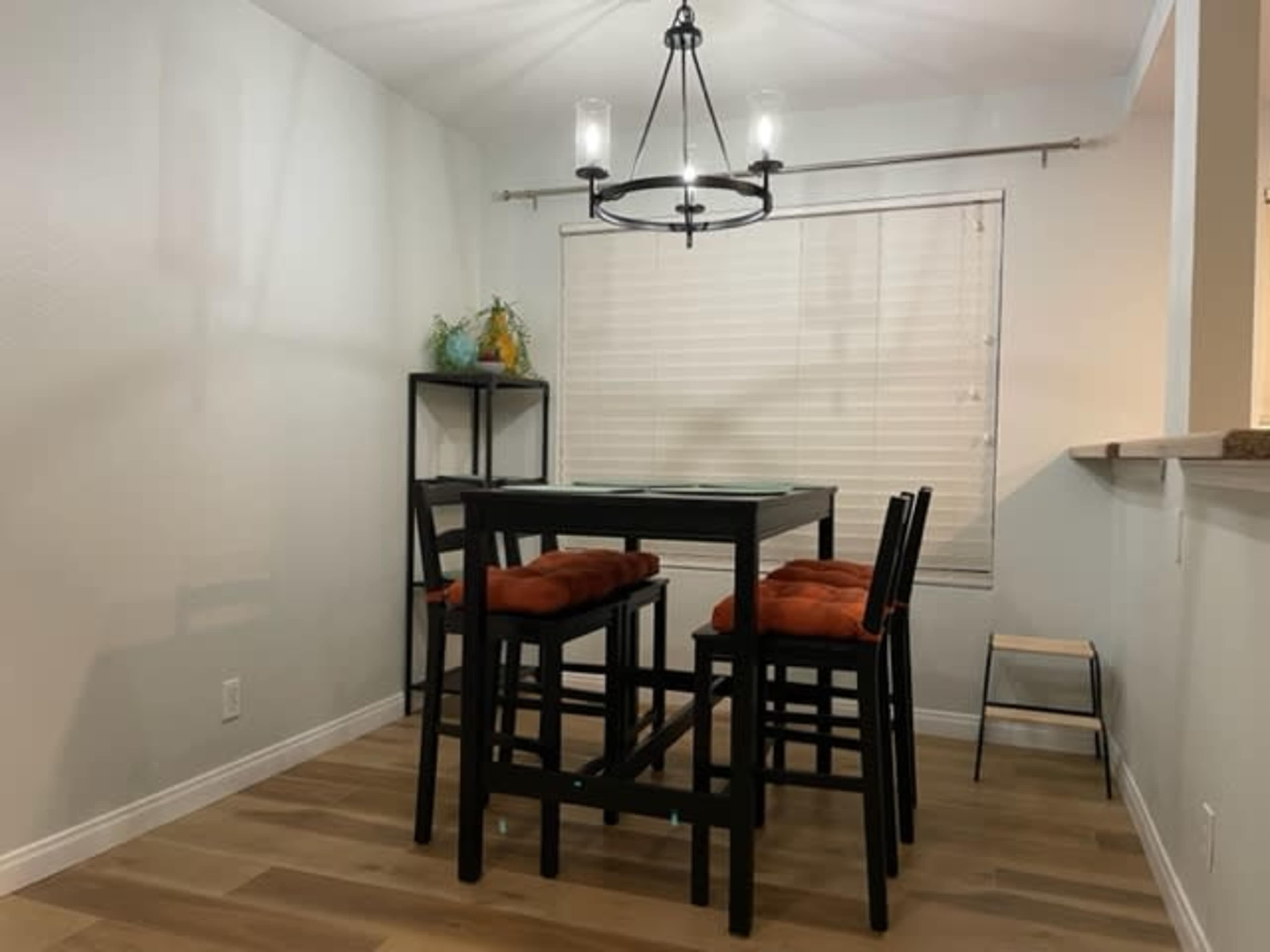A dining area features a table with black chairs and orange cushions, illuminated by a chandelier above.