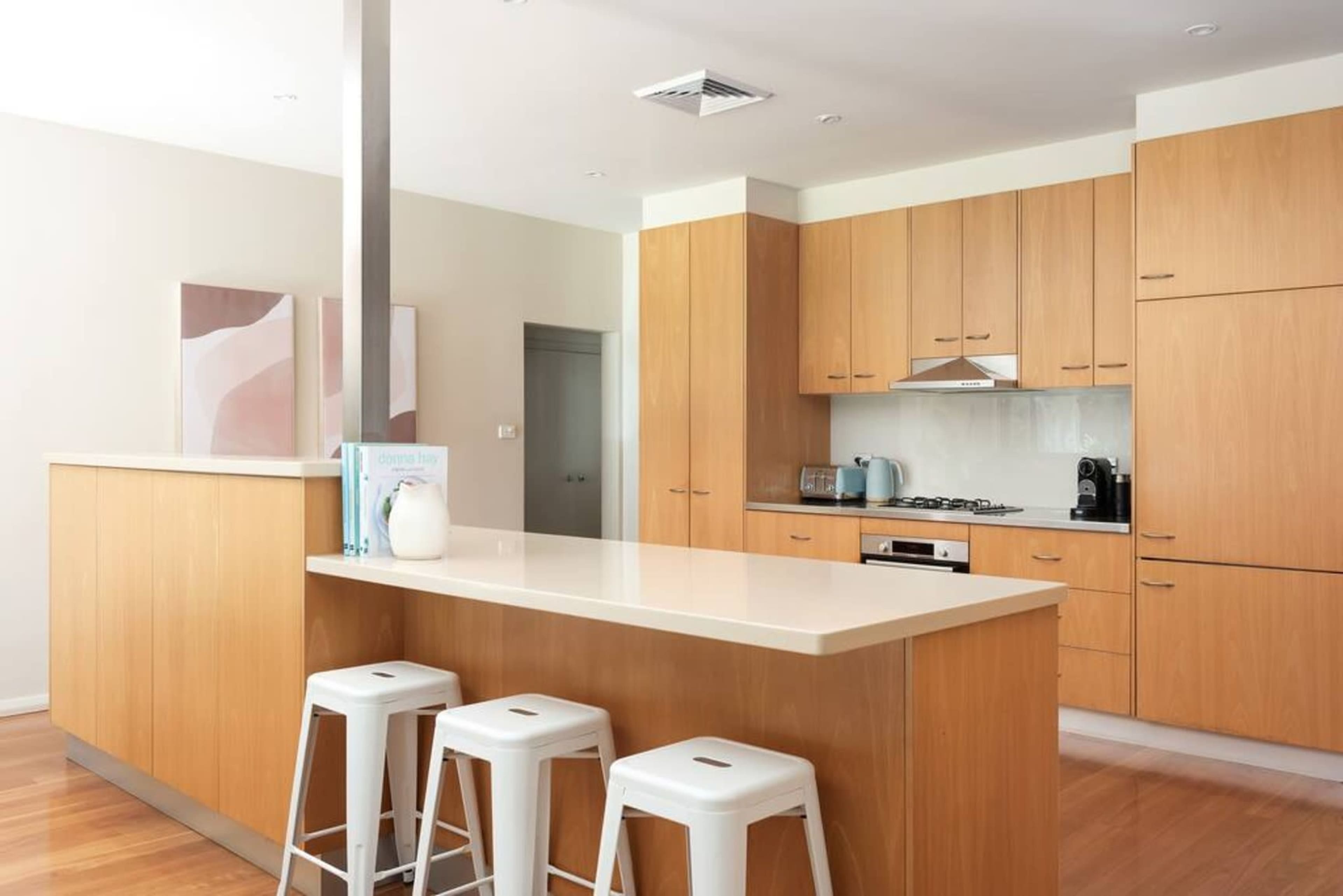 A modern kitchen featuring wooden cabinets, a white countertop, and three white stools at the island.