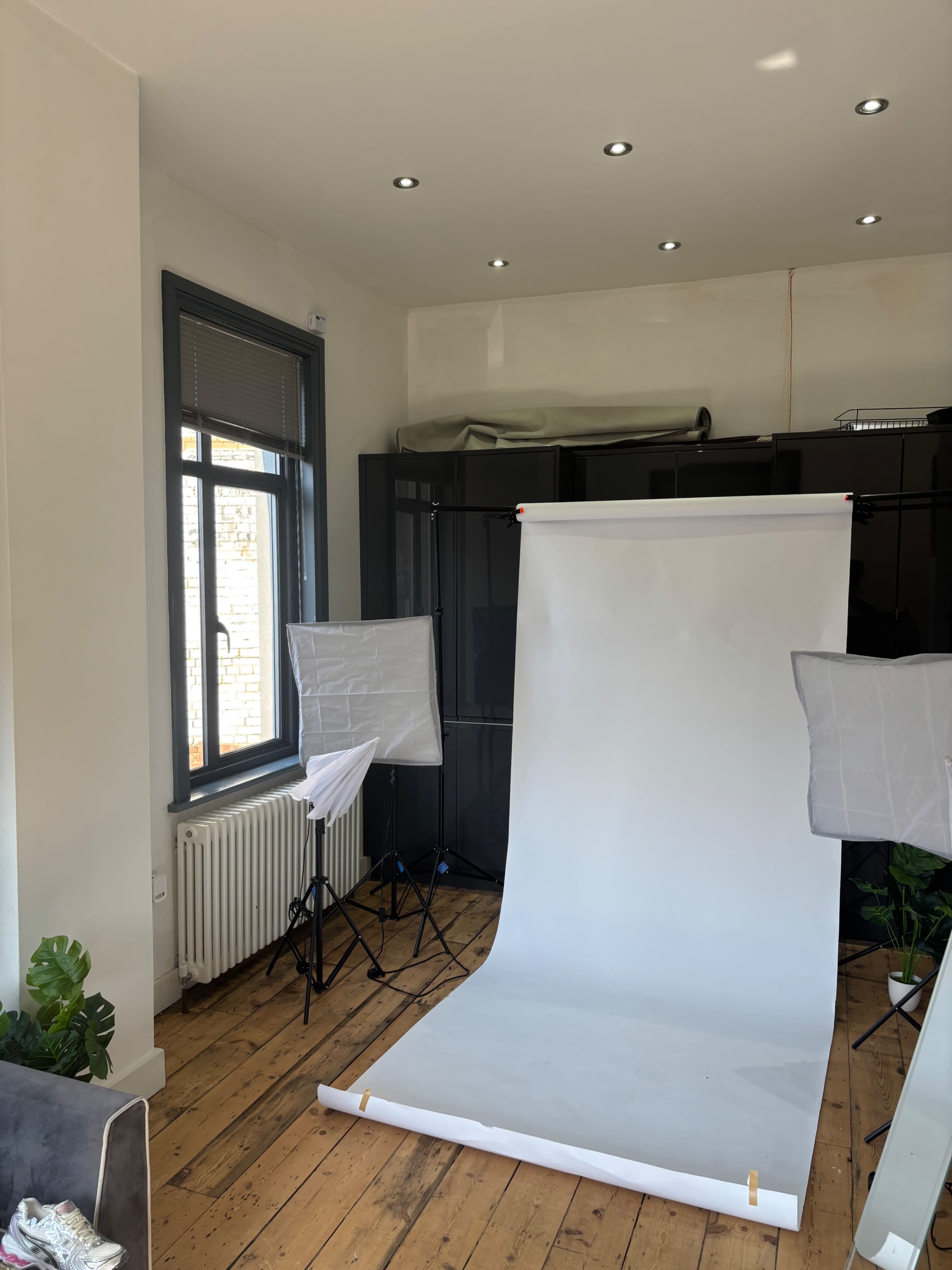 The image shows a photography setup with a white backdrop, two lighting softboxes, and hardwood floors in a well-lit room.
