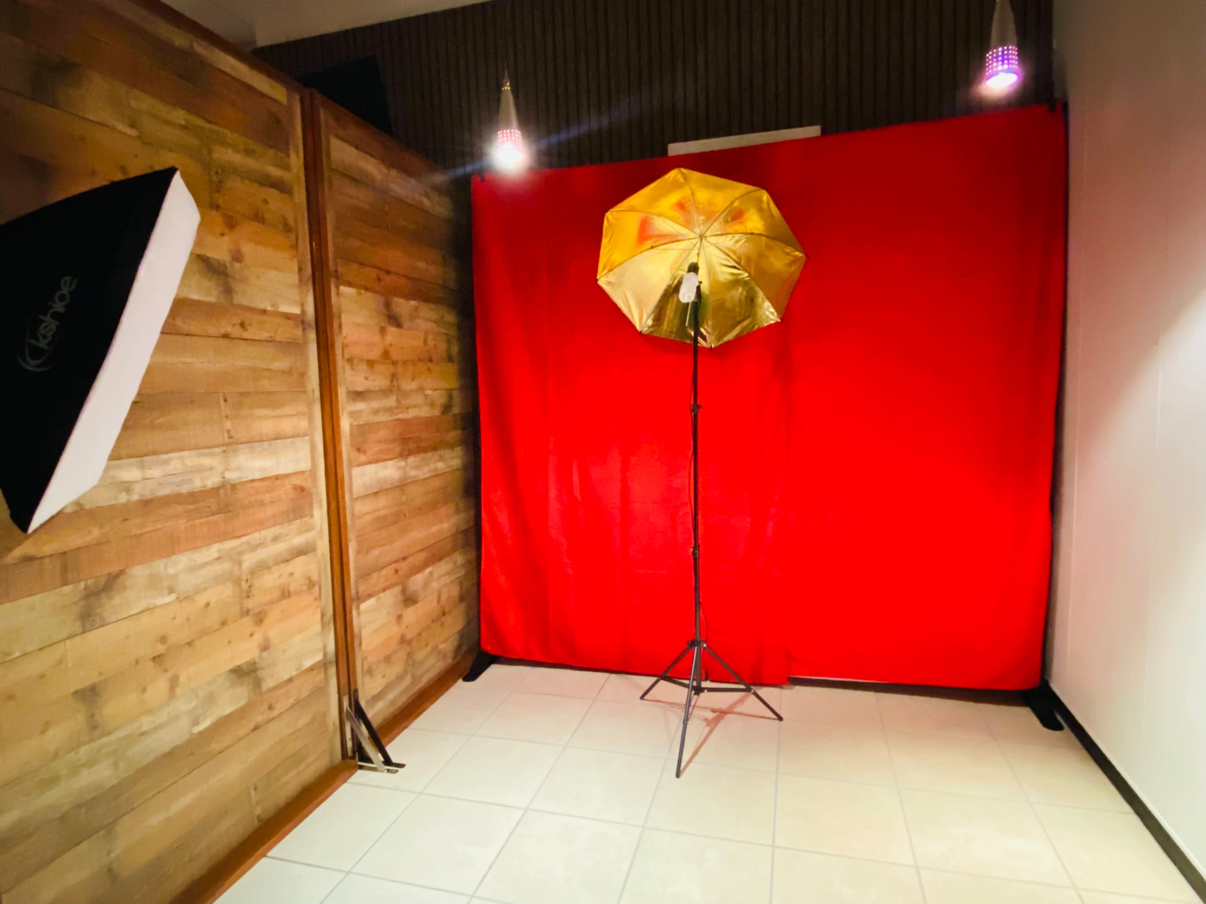 The scene features a photography setup with a red backdrop and a gold umbrella reflector on a stand.