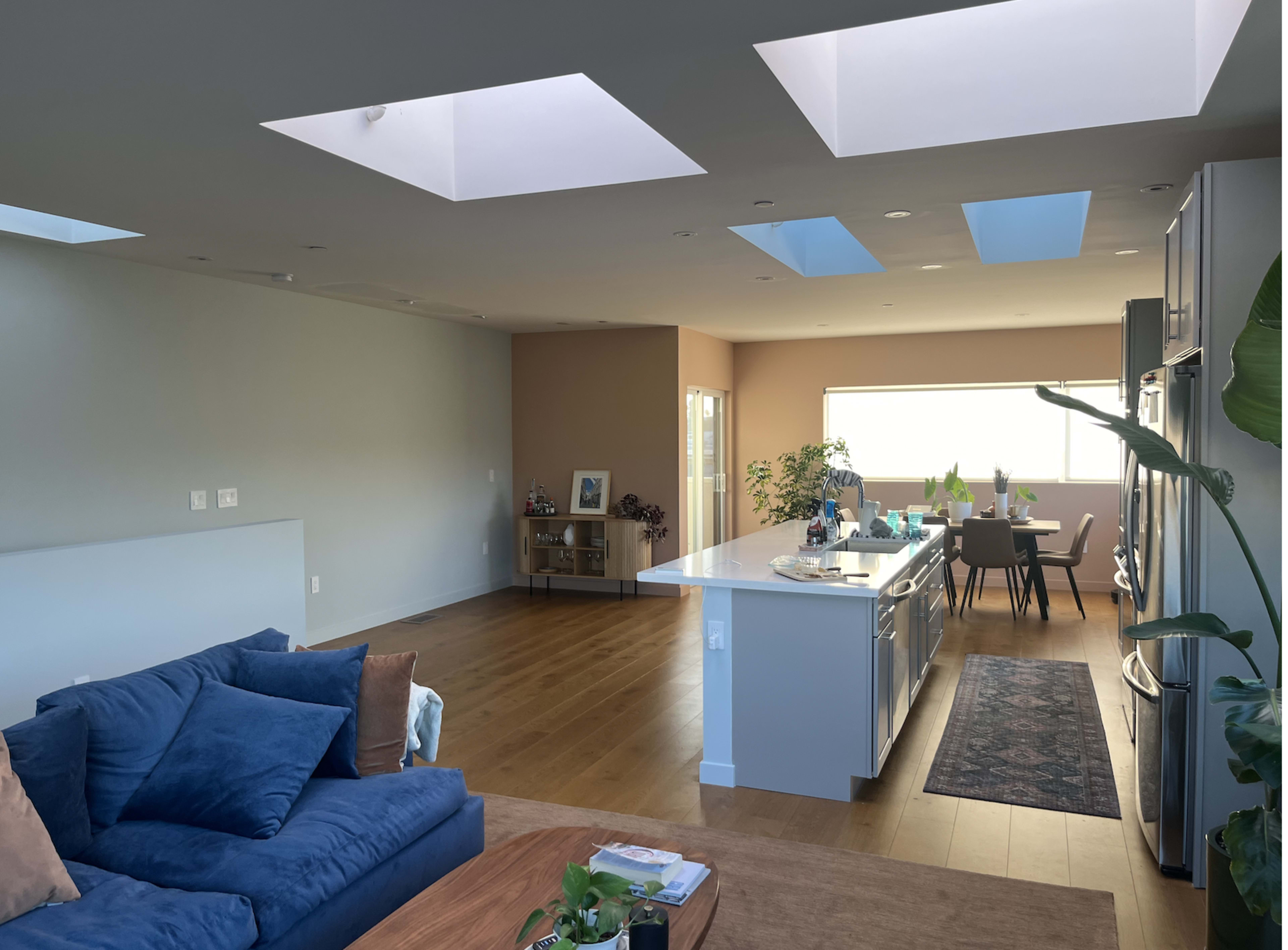 A modern open-plan living space features a kitchen with a central island and large windows, alongside a cozy seating area with a blue couch.