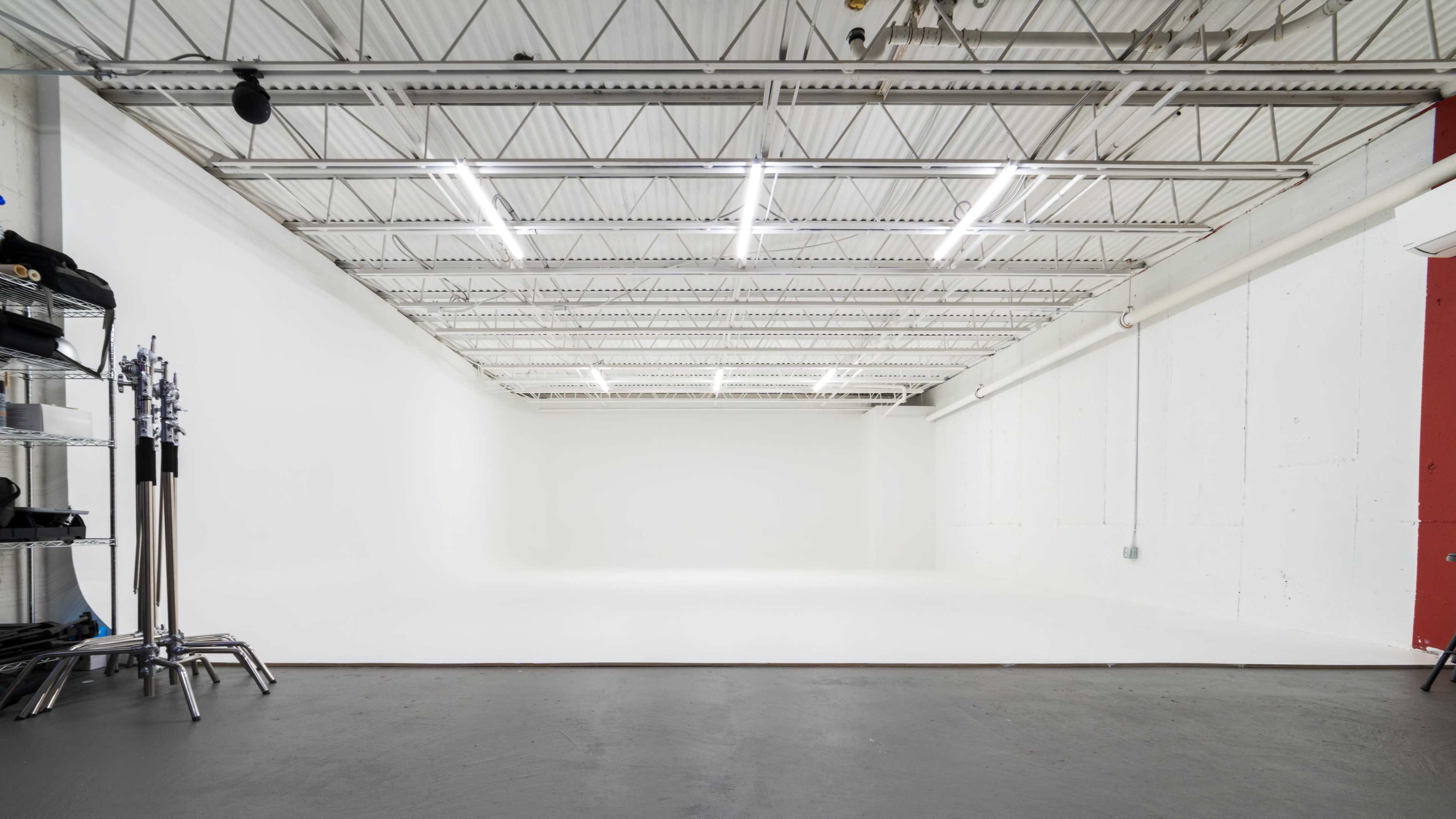An empty photography studio with a large white backdrop and overhead lighting.