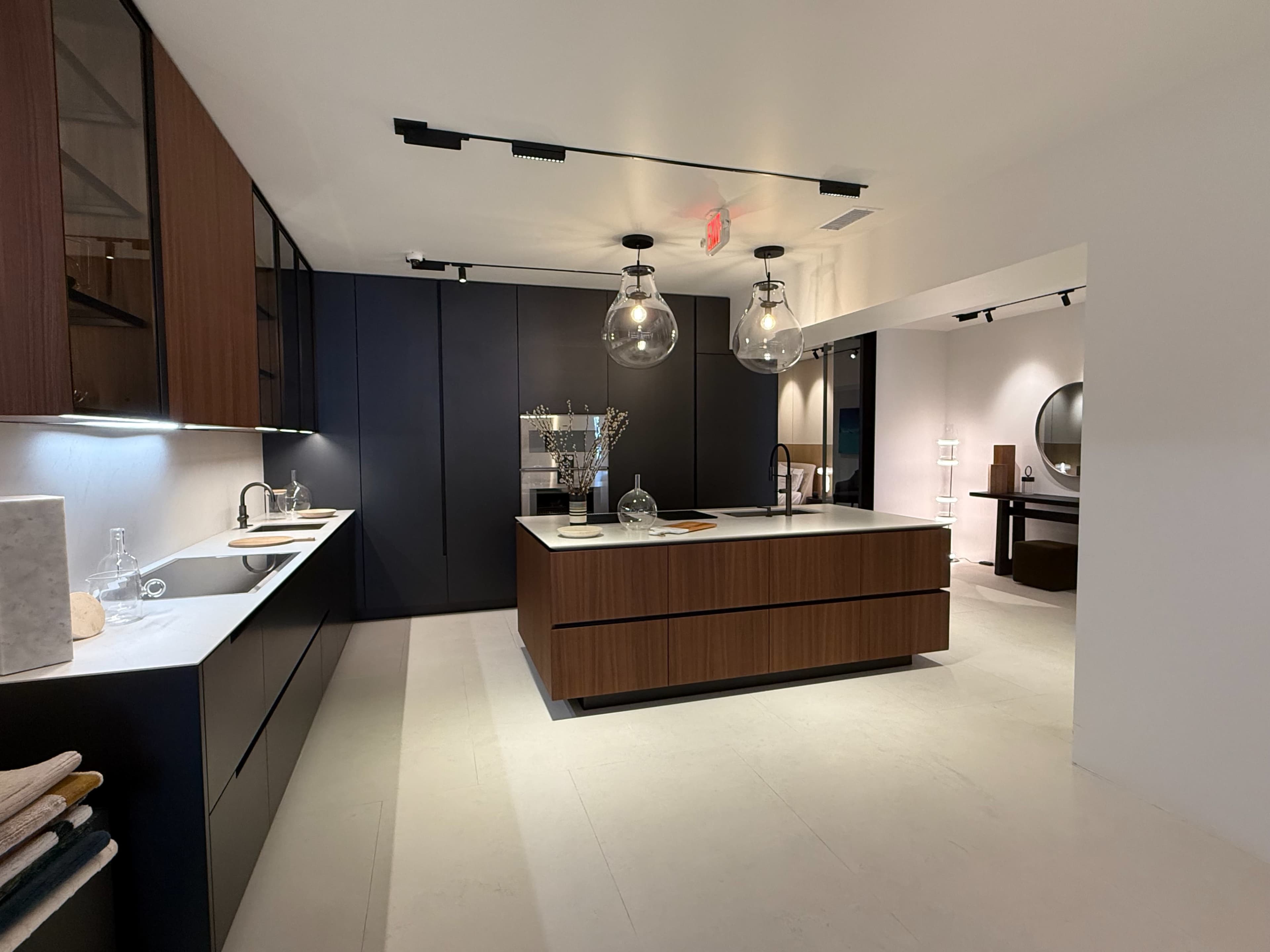 The image shows a modern kitchen featuring a large island with a wood finish, sleek cabinetry in dark tones, and pendant lighting.