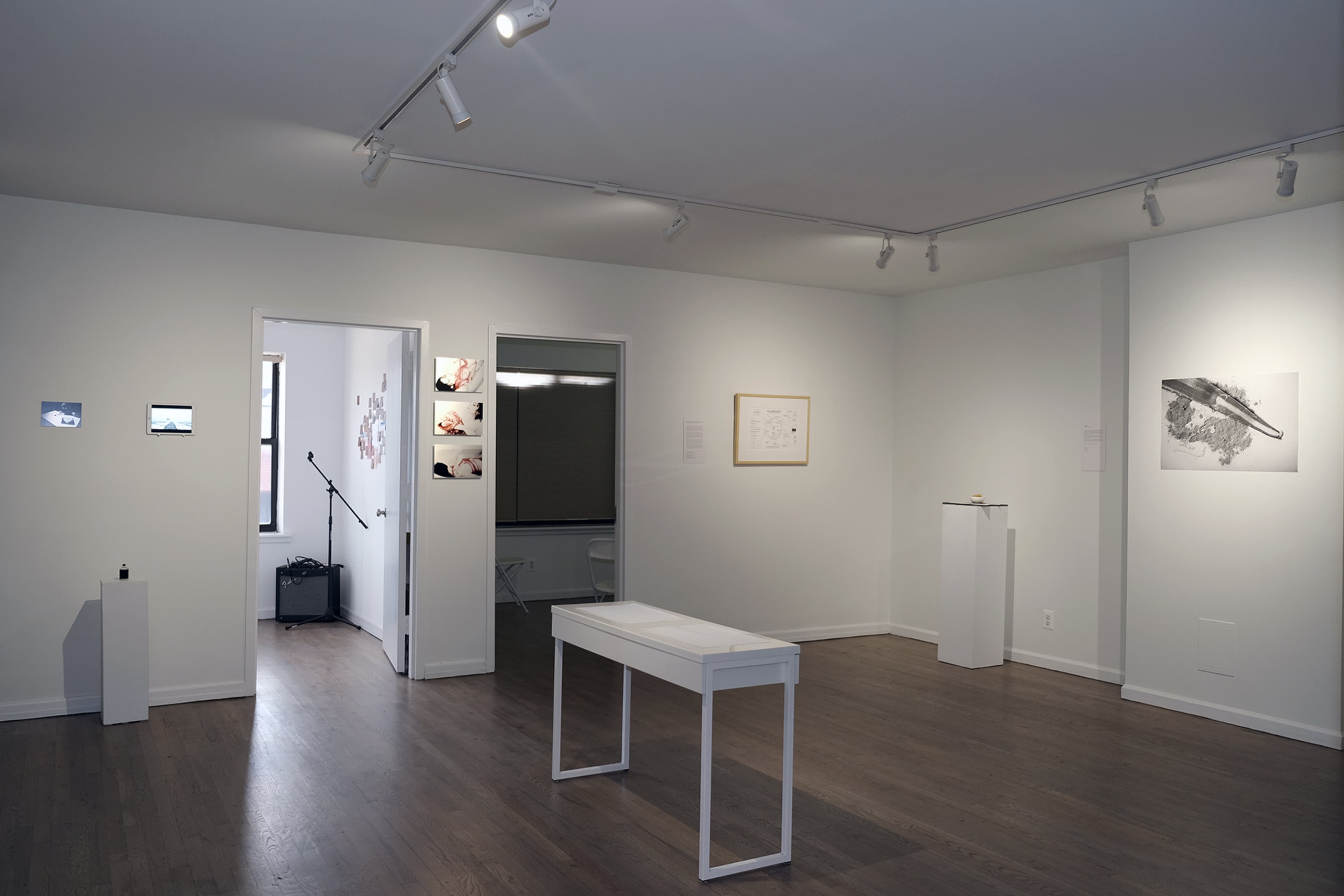A modern art gallery with white walls, a central white table, and various artworks displayed on the walls.