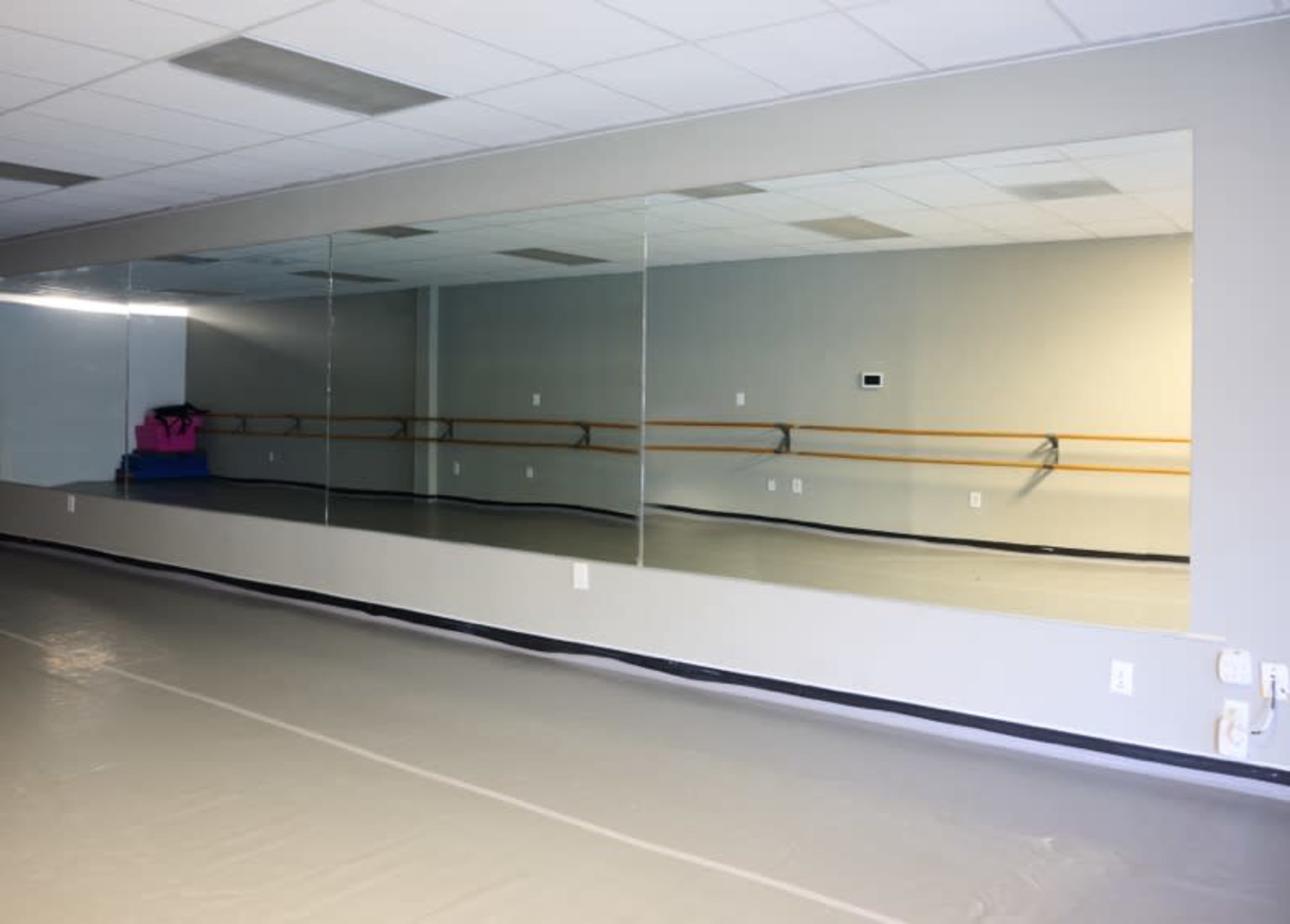 A spacious dance studio featuring a long mirror along one wall and ballet bars mounted on the adjacent wall.