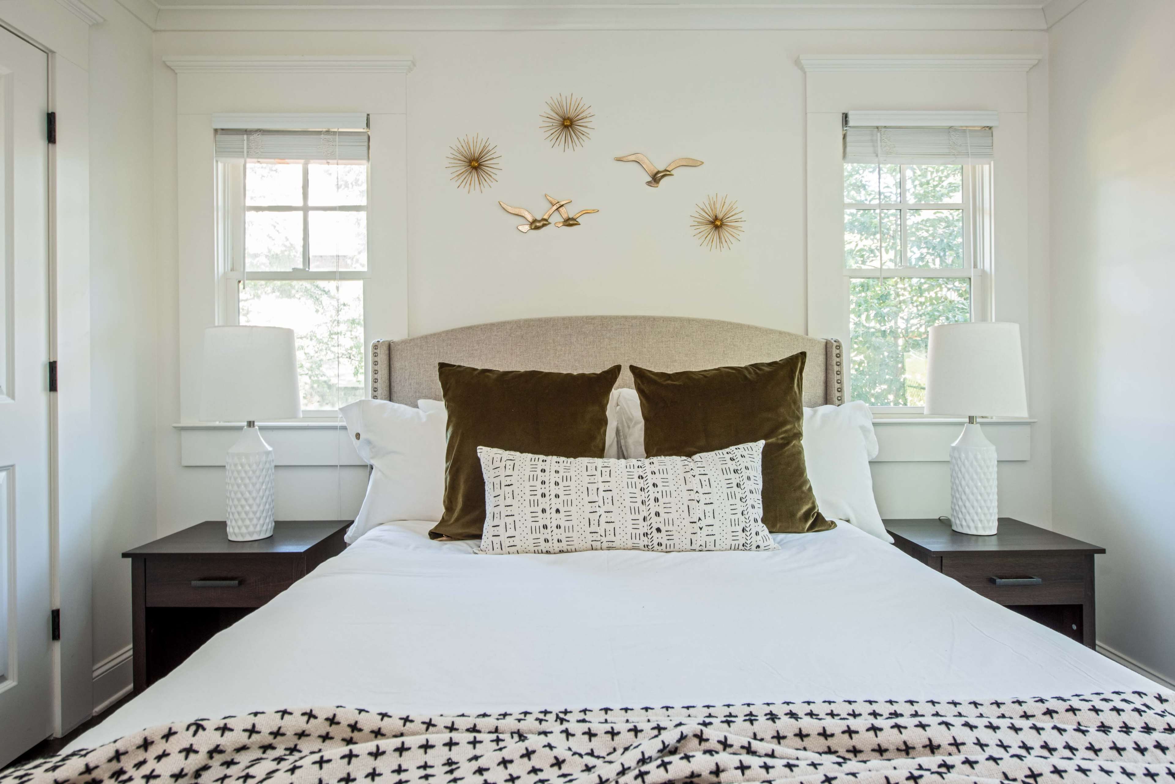 A neatly arranged bedroom featuring a bed with a headboard, two bedside tables with lamps, and decorative wall art.