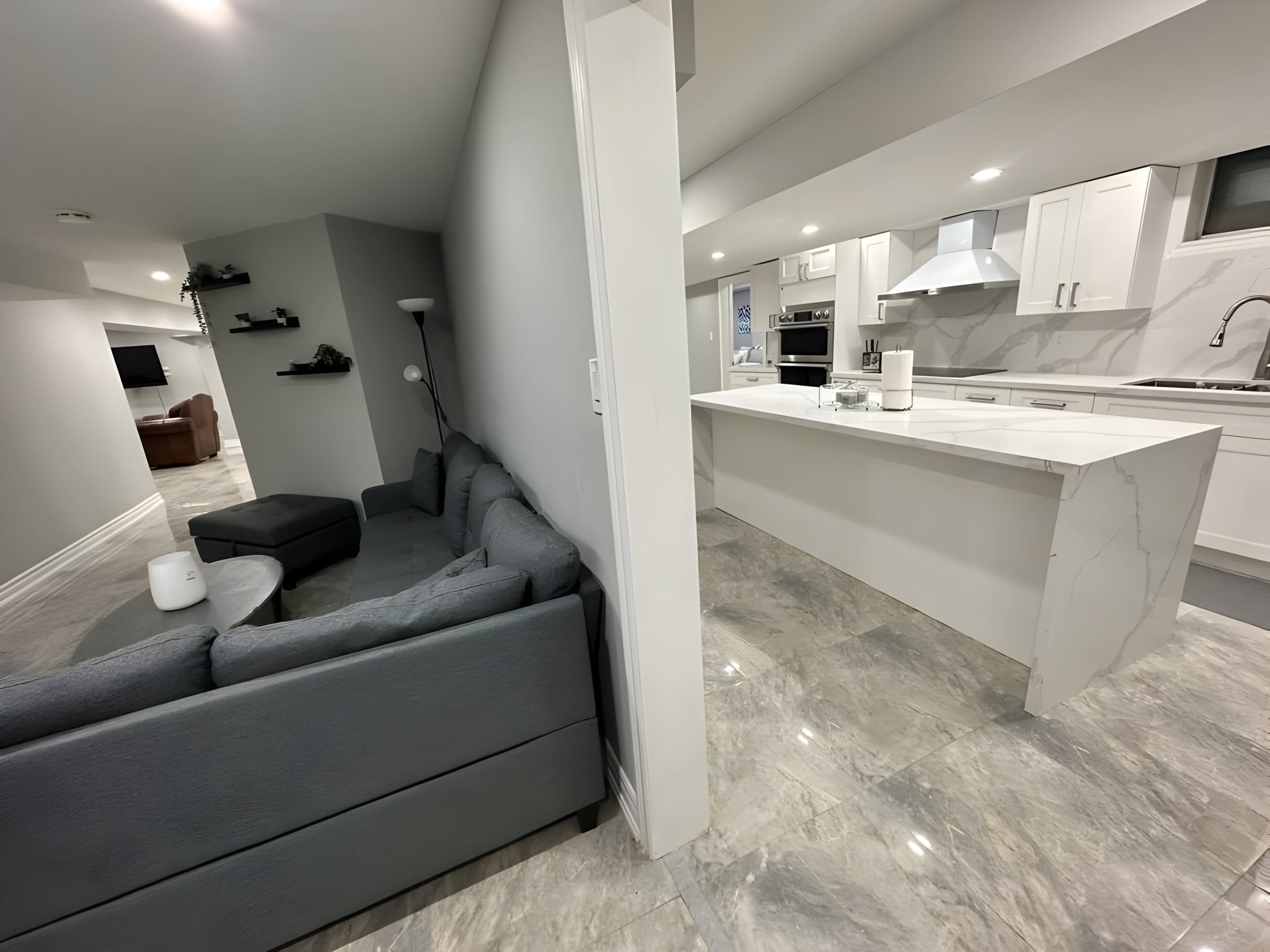 A spacious modern kitchen adjacent to a living area featuring a gray couch and minimalist decor.