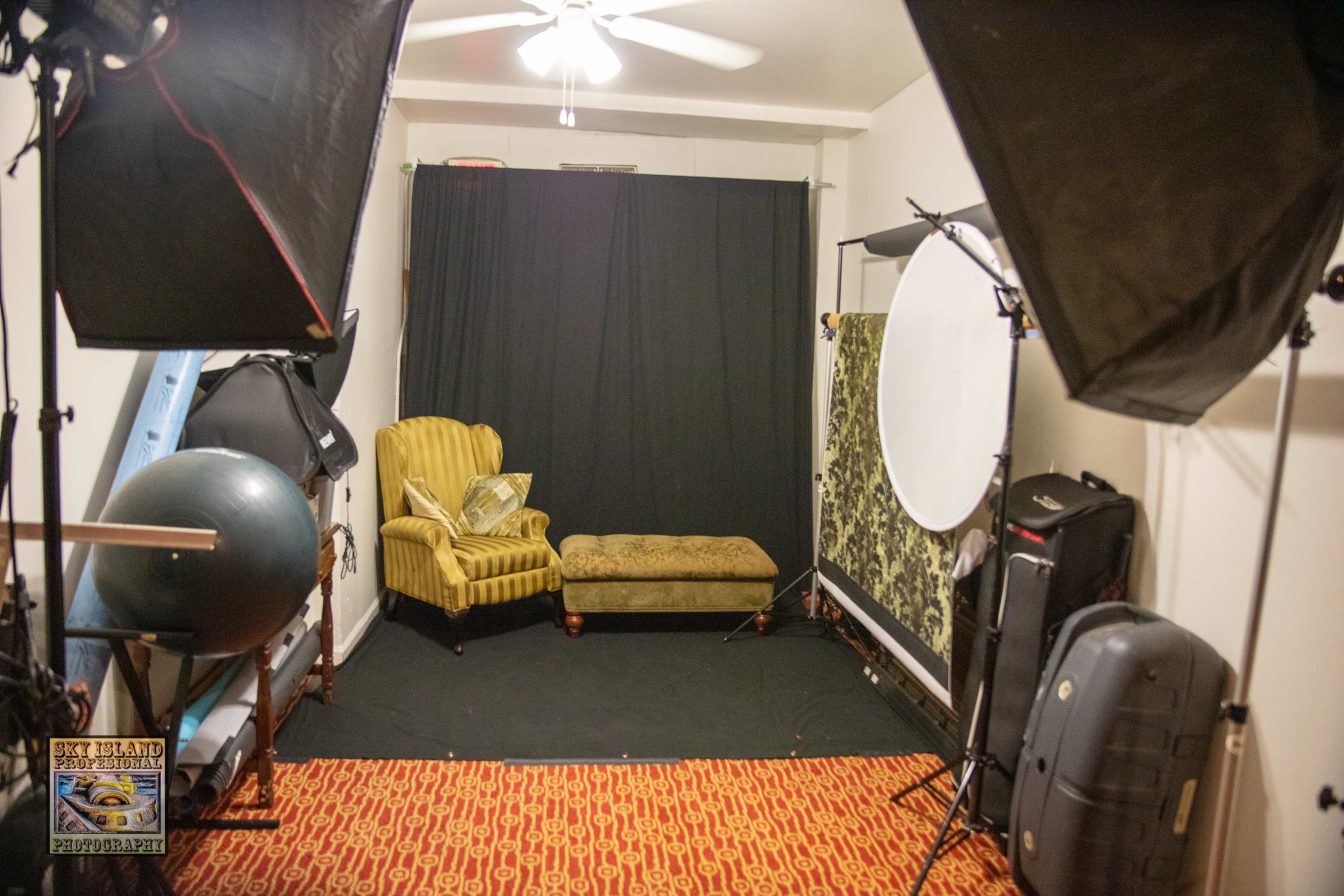 A photography studio with a green velvet couch, a black backdrop, and various studio lighting equipment.