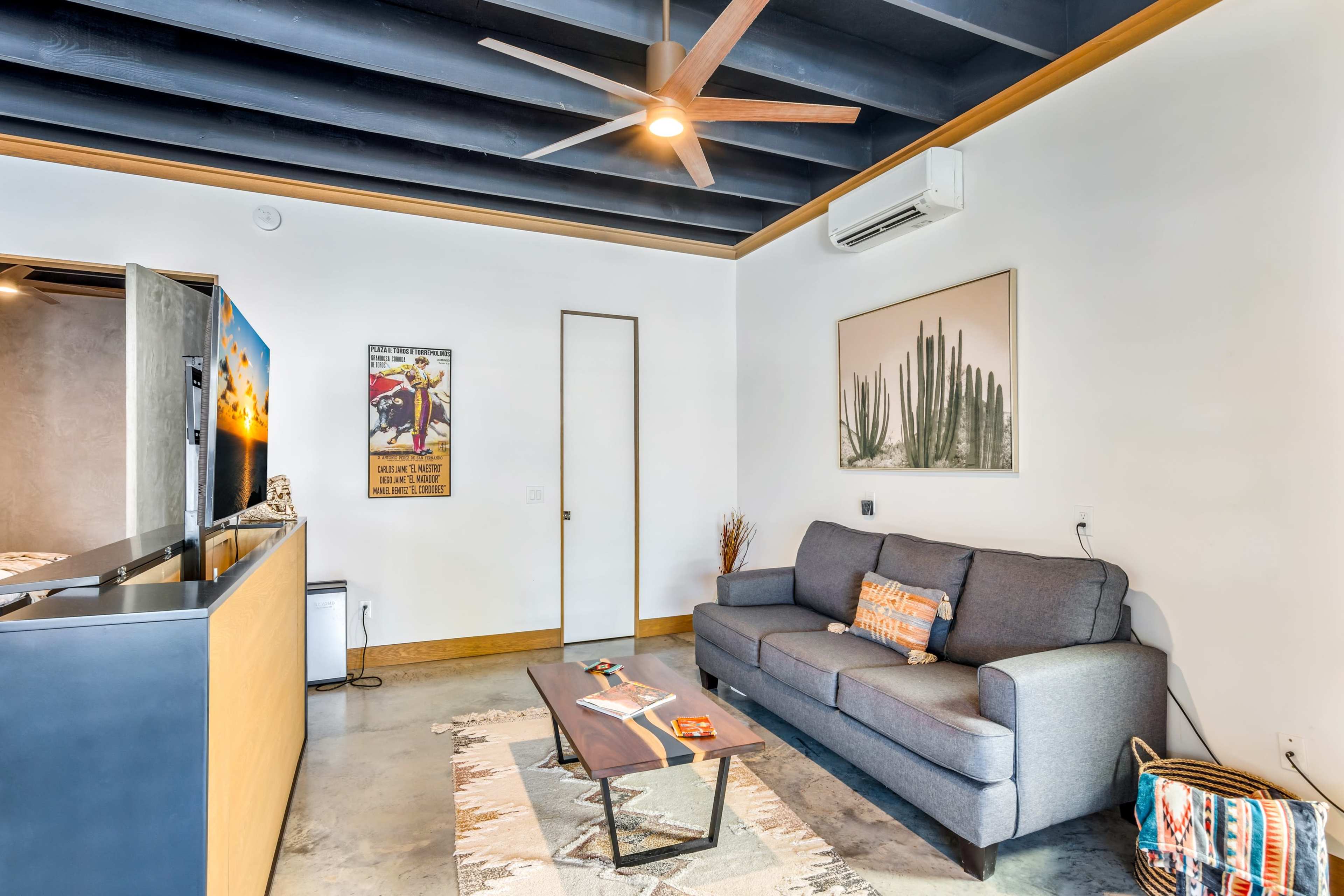 A contemporary living room with a gray sofa, a coffee table, a ceiling fan, and decor featuring a cactus and western-themed artwork.
