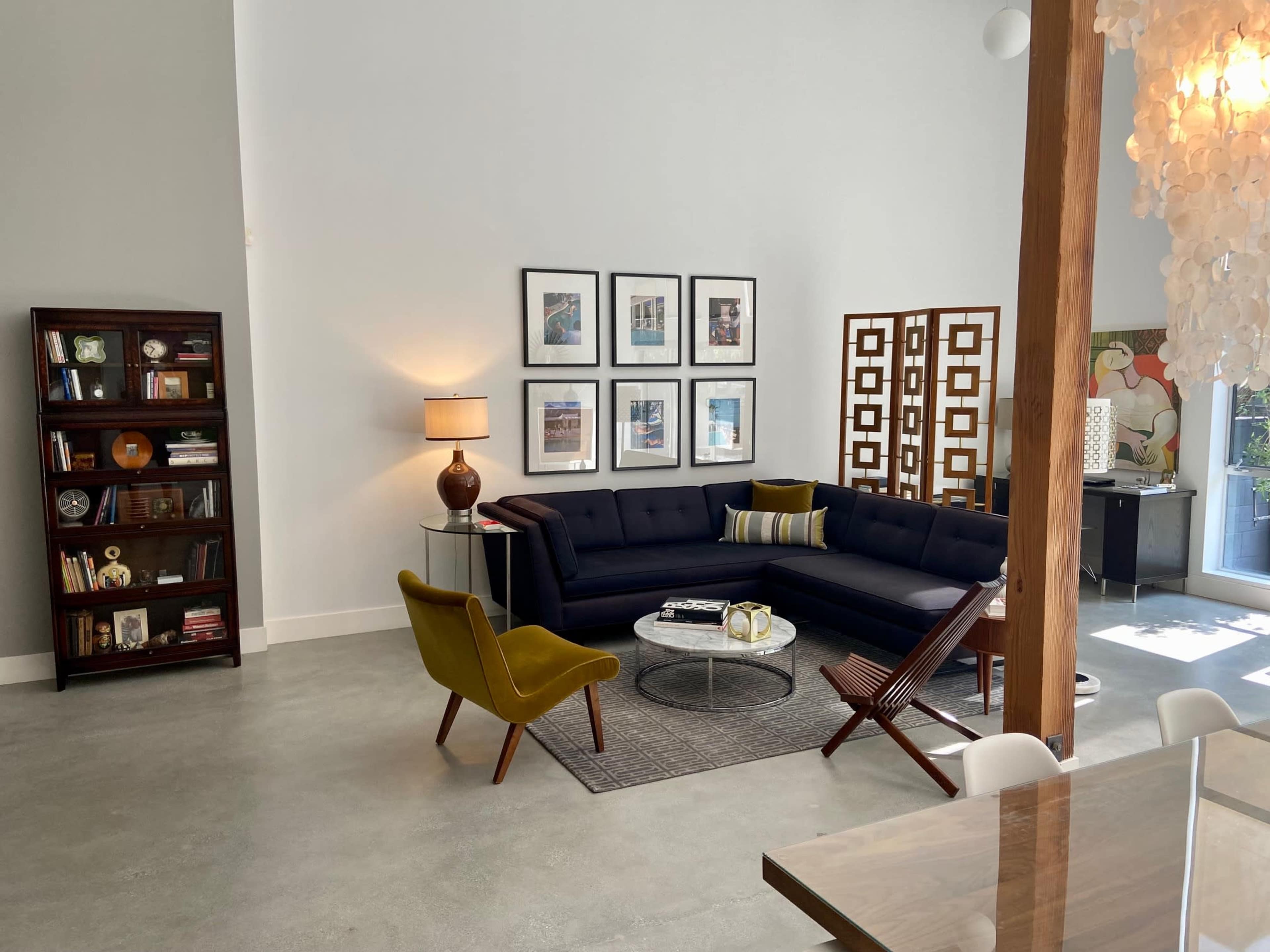 A modern living room features a dark sectional sofa, a round coffee table, and a bookshelf, accented by a floor lamp and decorative artwork.