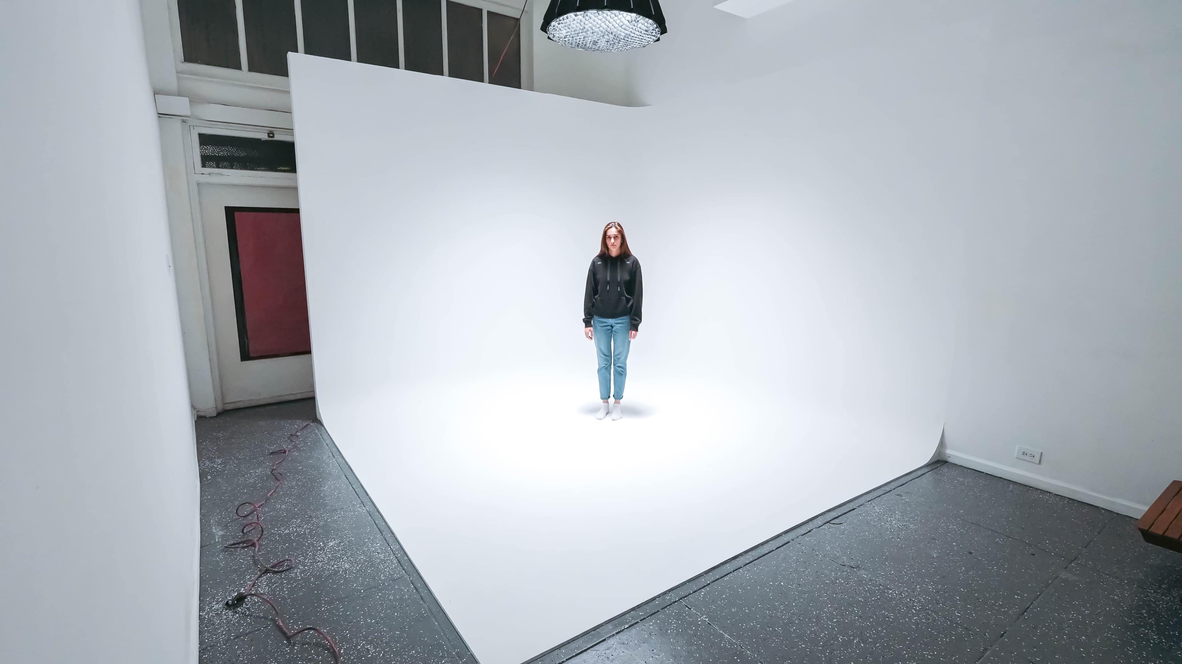 A person stands on a white floor in a brightly lit room with white walls and minimal furnishings.