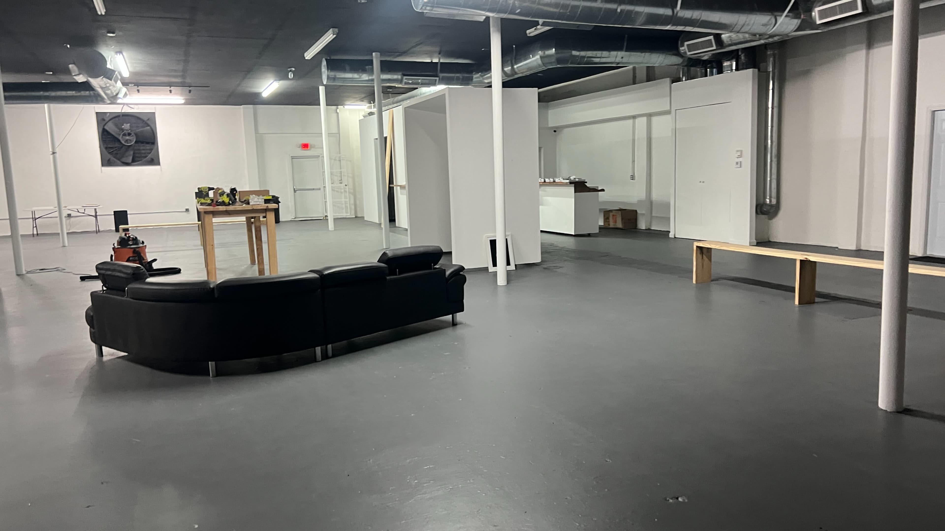 A spacious, empty room with a black sectional sofa, a wooden table, and white partitions along the walls.