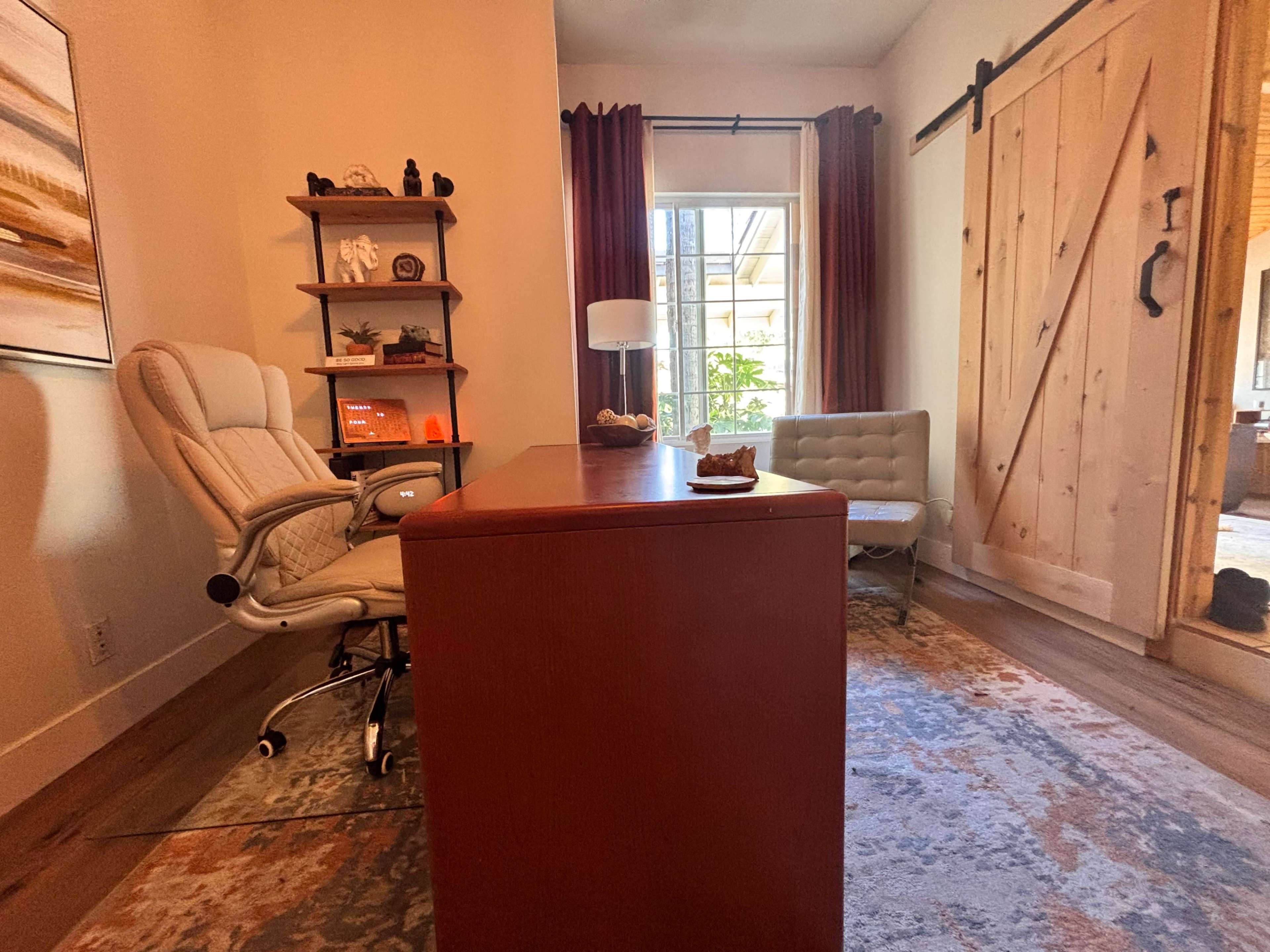 The image shows a modern office space with a desk, ergonomic chair, shelving unit, and a light-colored sofa, complemented by wooden sliding doors and natural light.