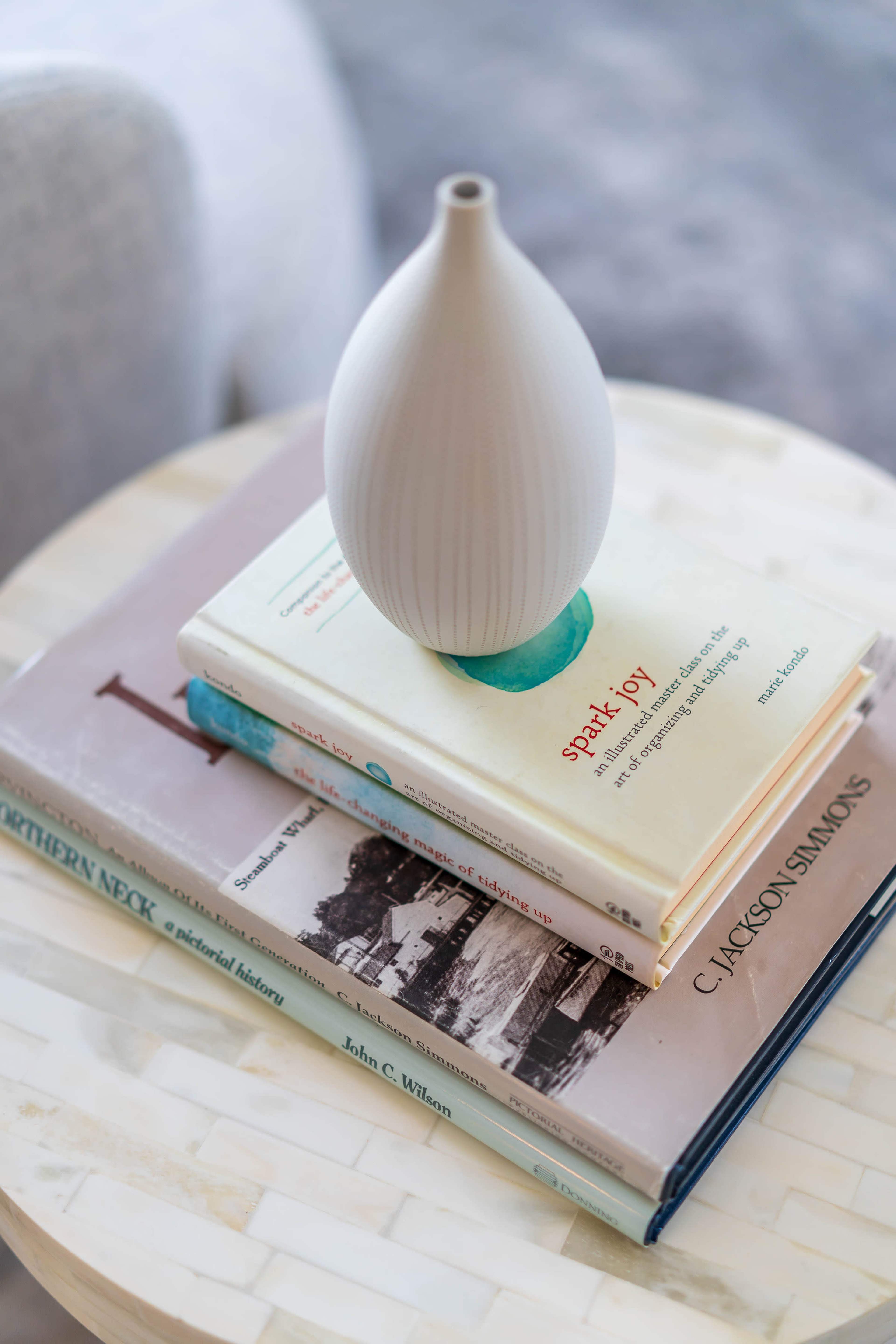 A white vase sits atop a stack of three books on a round table.