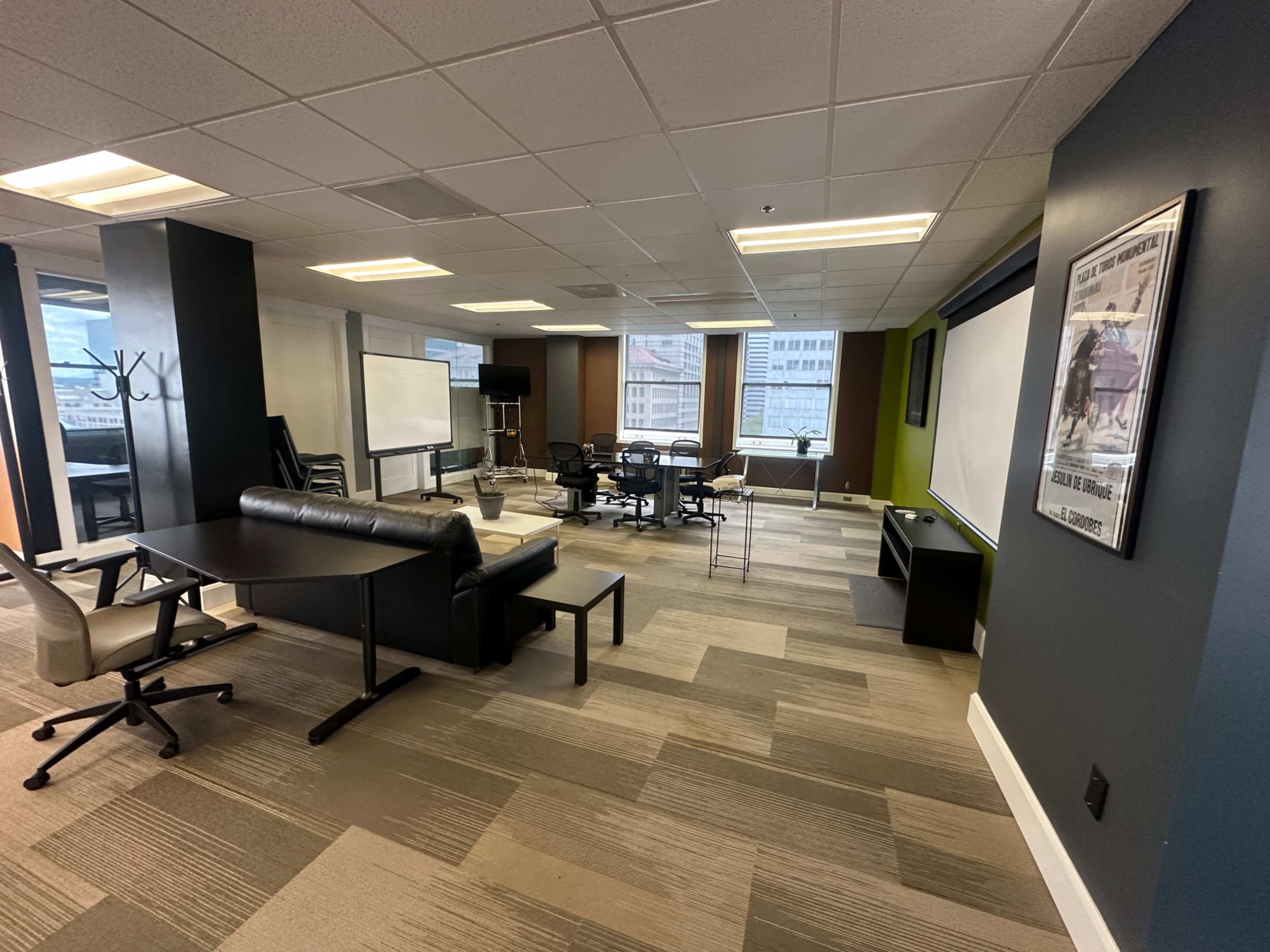 The image shows a modern office space featuring a mix of seating areas, a conference table, and large windows with a city view.