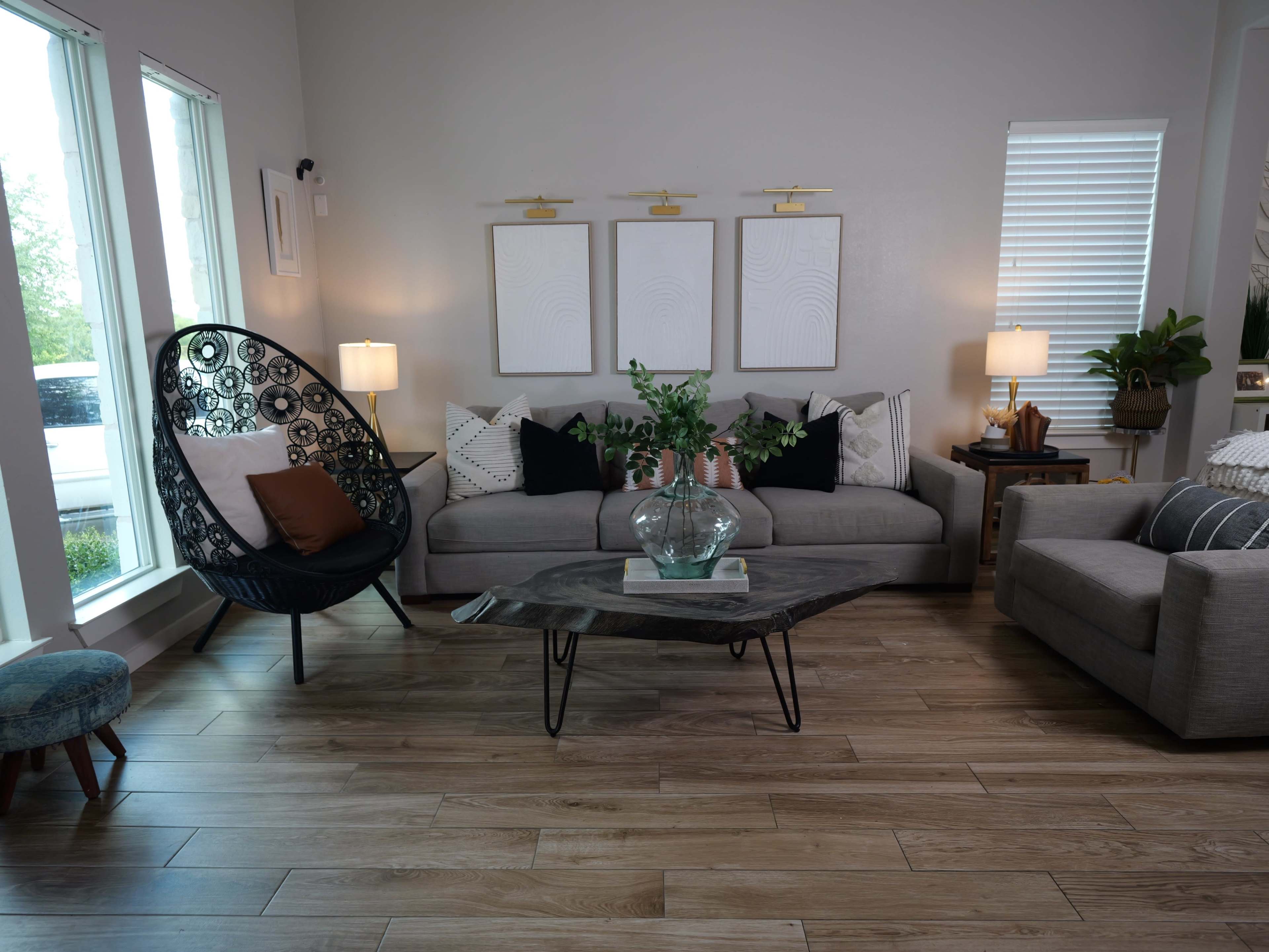 The living room features a gray sectional sofa, an organic-shaped wooden coffee table, and a large decorative chair, complemented by large windows and a minimalist decor style.