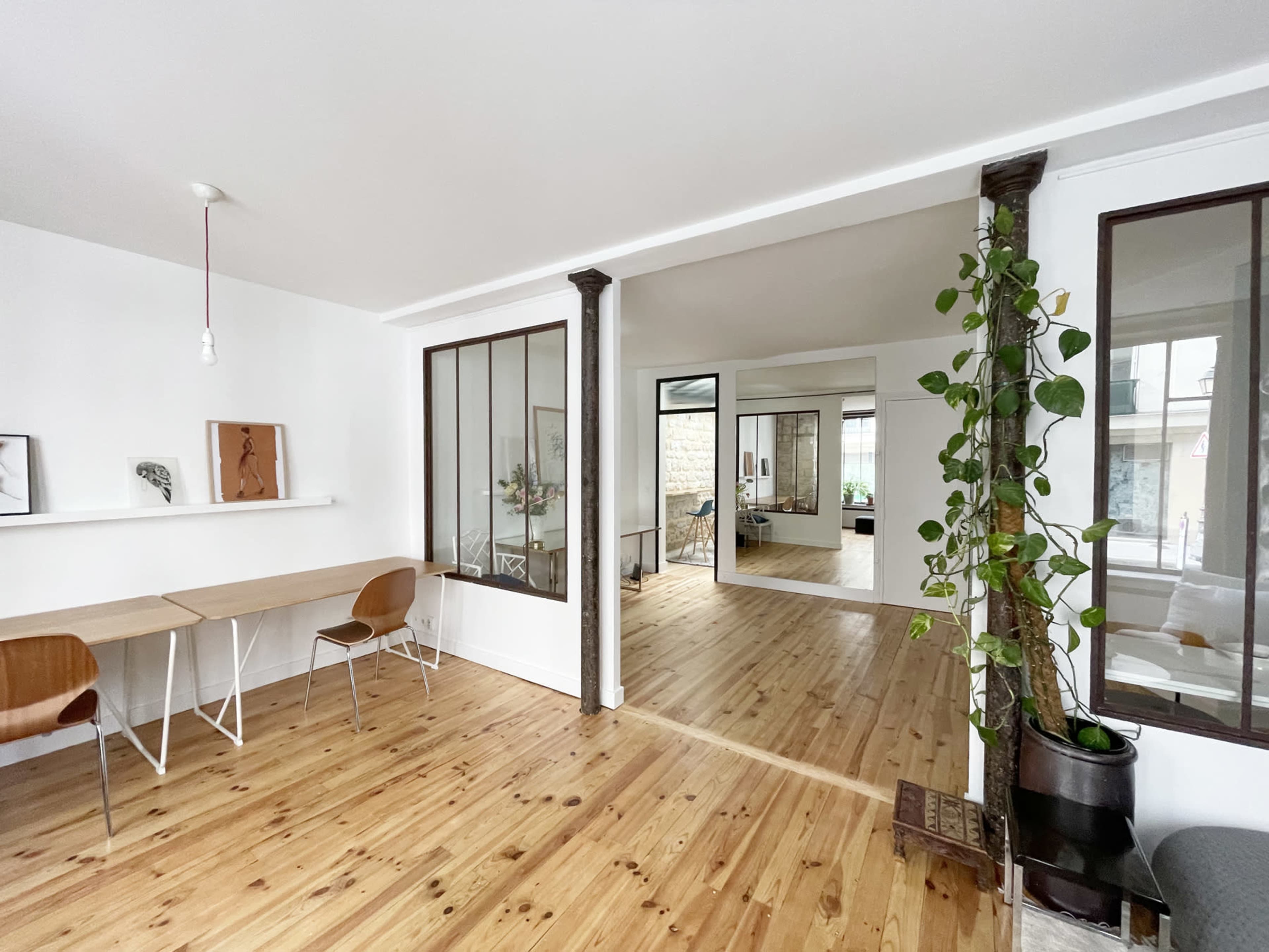 A modern, open-concept interior with wooden floors, a small workspace area with two chairs, and a glass partition leading to another room.