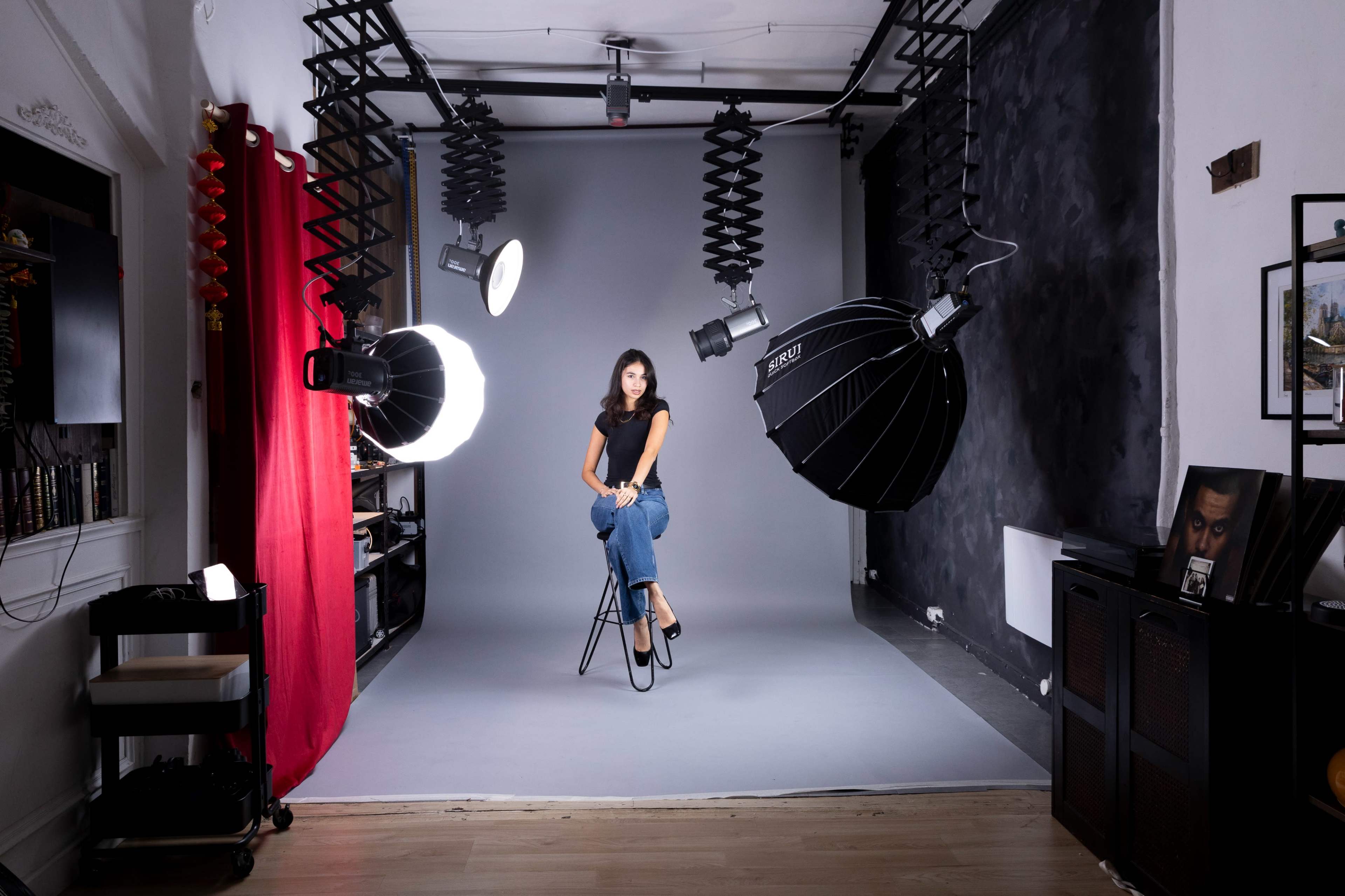 A woman sits on a stool in a photography studio, surrounded by large softbox lights and a gray backdrop.