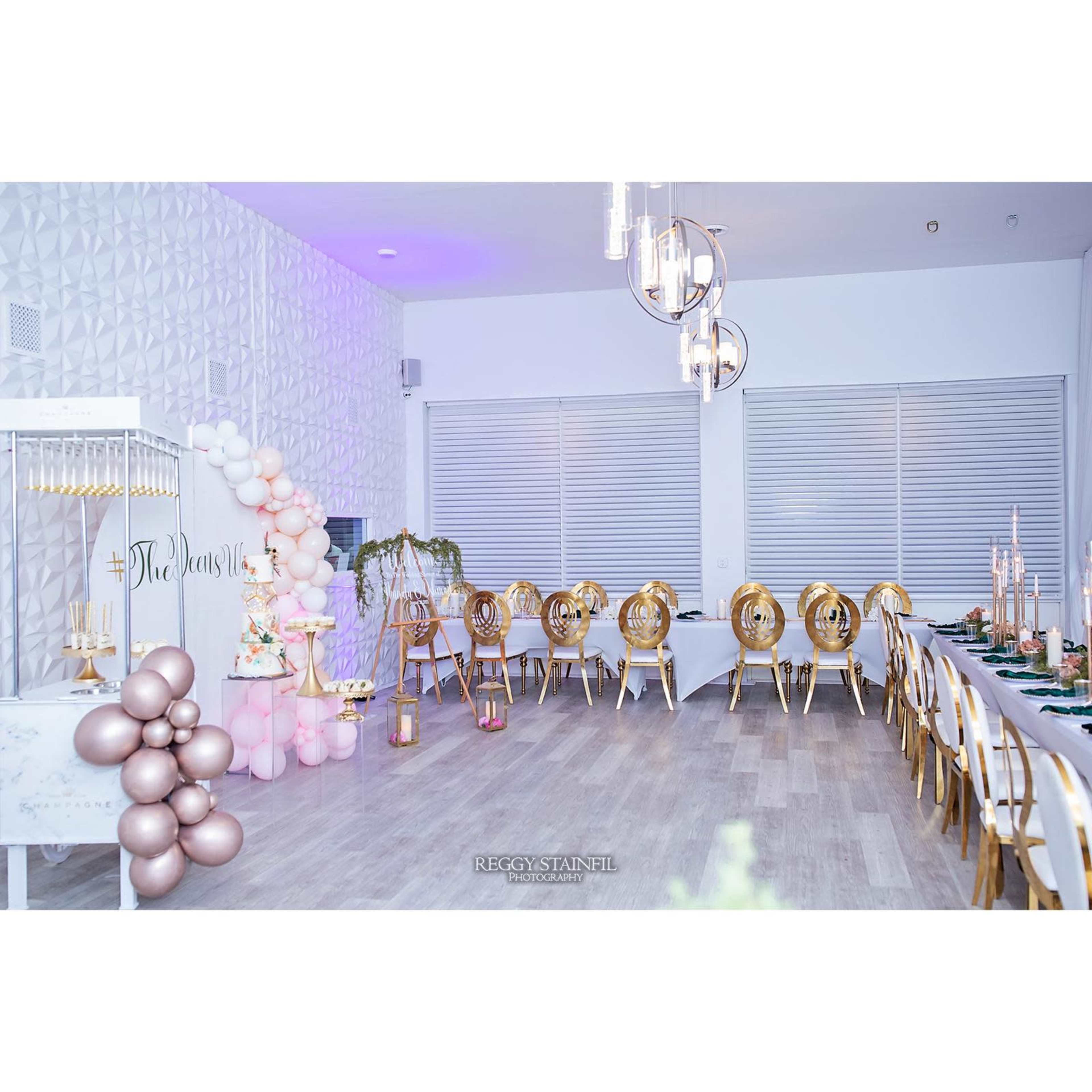A decorated indoor venue featuring elegant seating arrangements, a balloon arch, and a table set for an event.