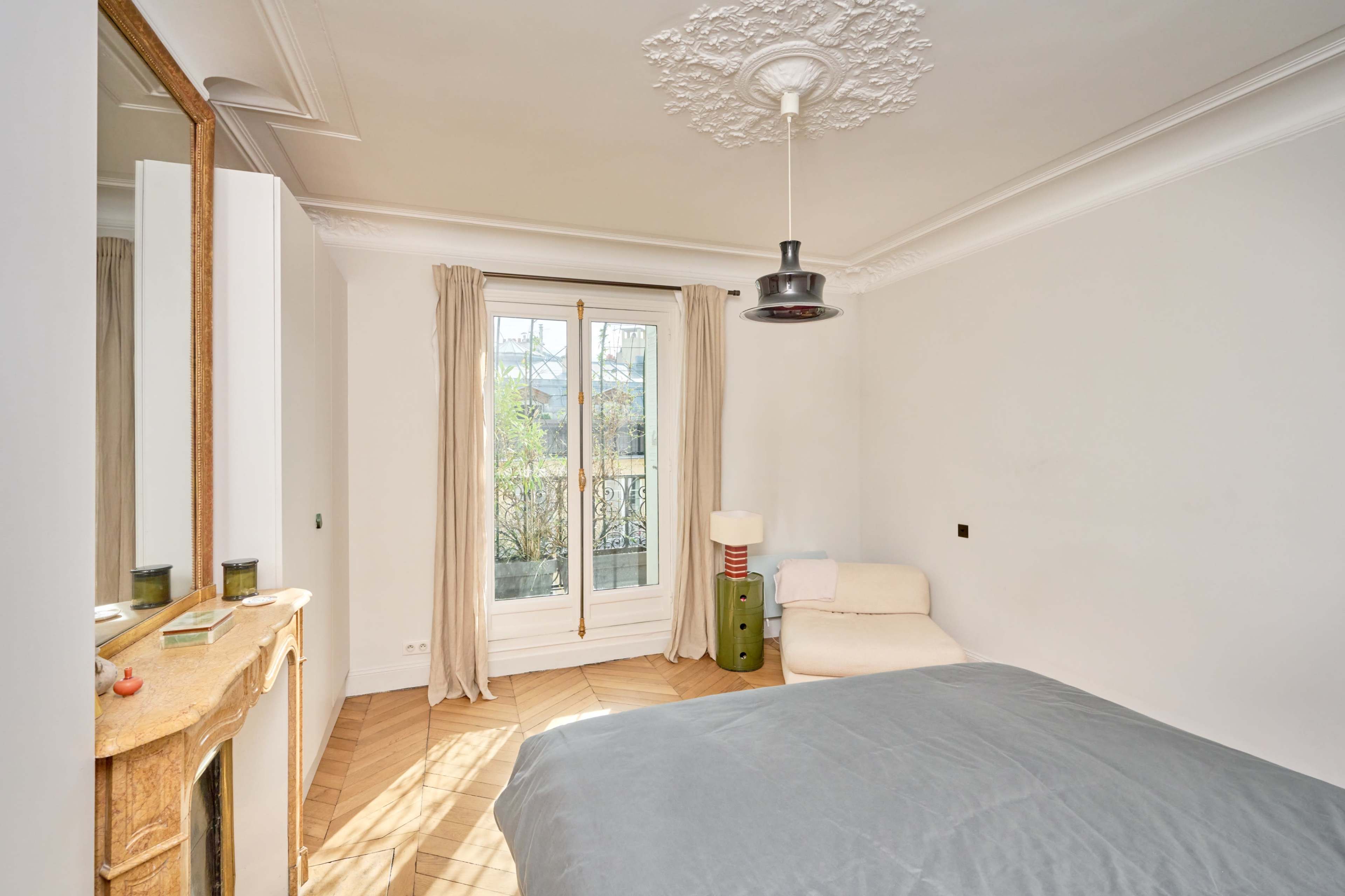 The room features a bed, a chair, and a decorative fireplace with a large window that opens to a view outside.