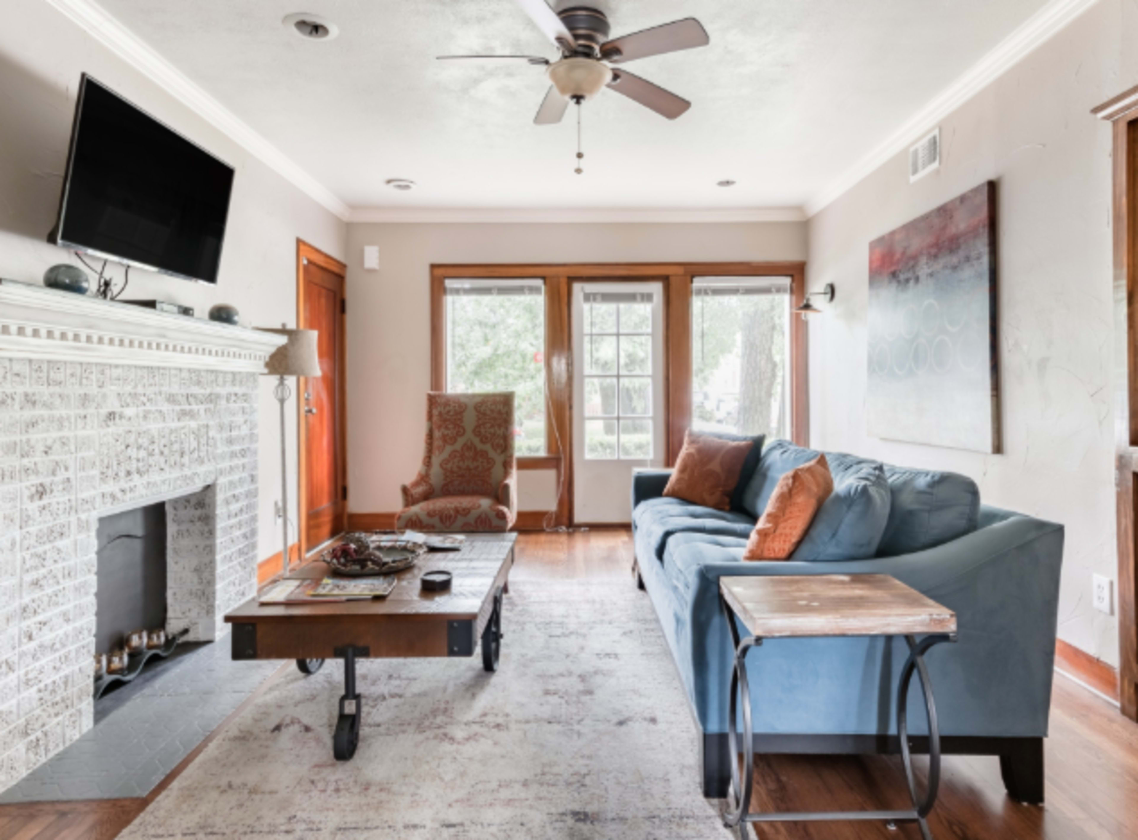 A living room features a blue sofa, a wooden coffee table, an armchair, and a fireplace with a television mounted above it.