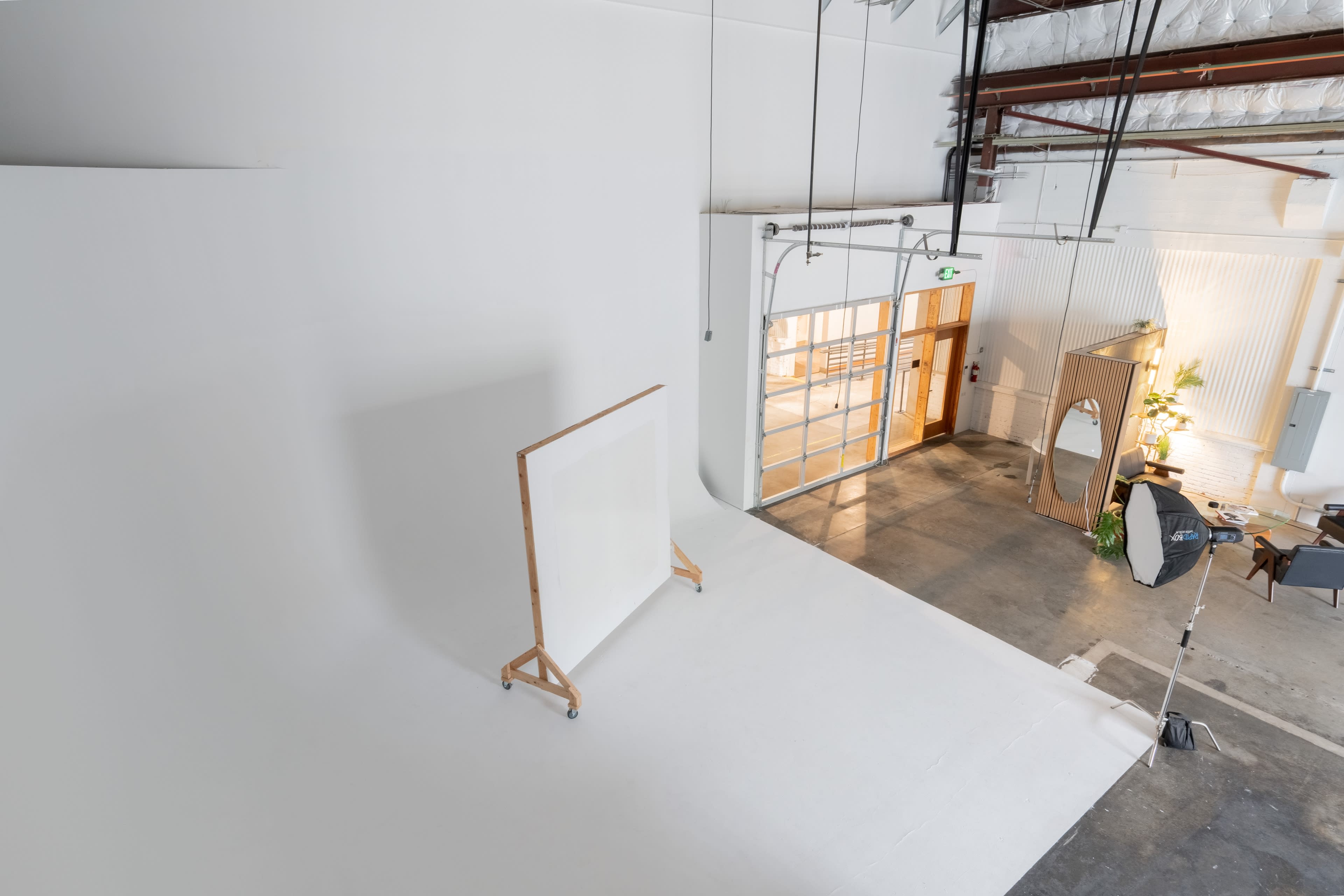 The image shows a spacious, well-lit studio with a large white backdrop and an entrance featuring glass doors.