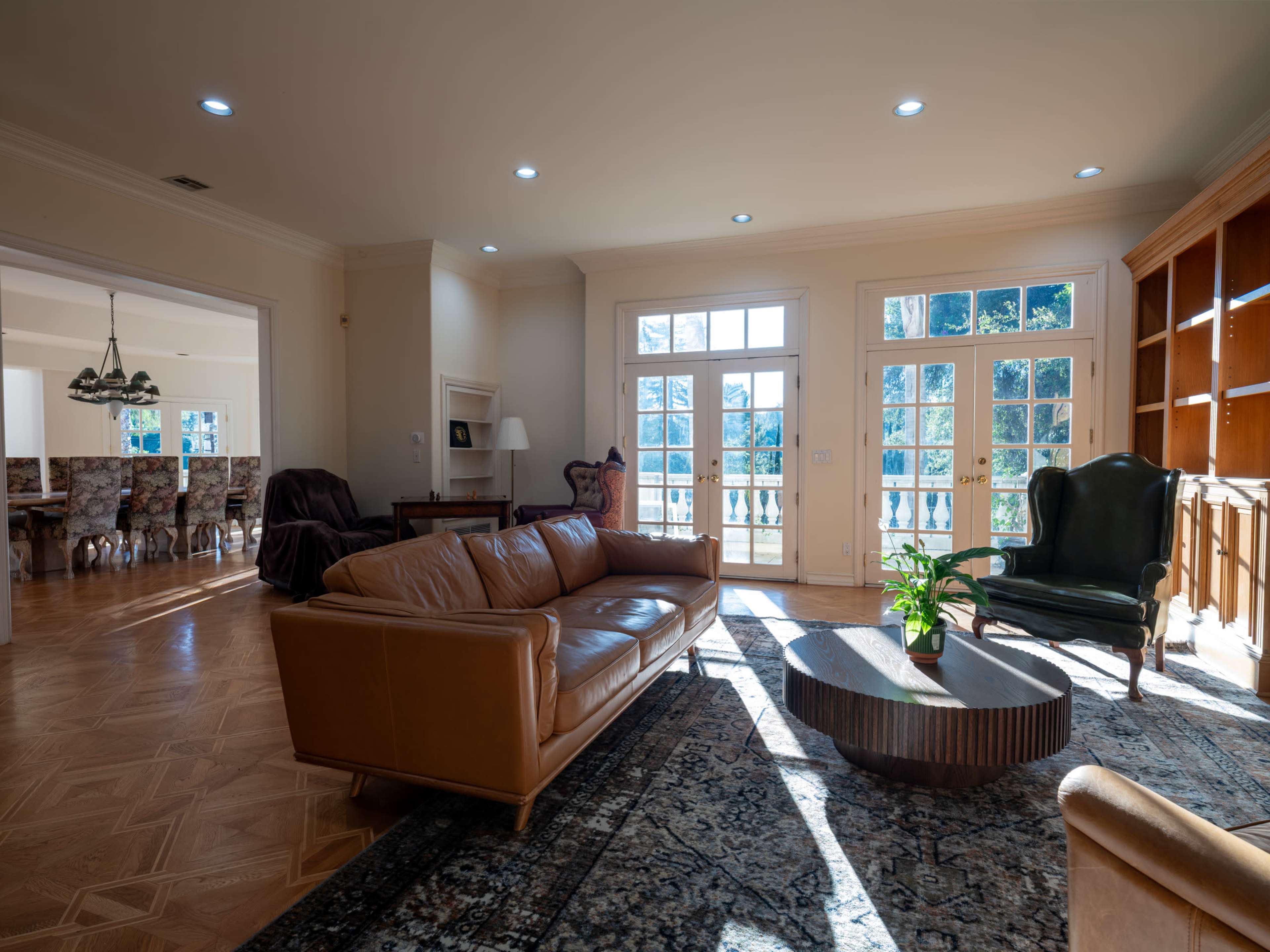 The image shows a spacious living room with a leather sofa, a round coffee table, and large windows letting in natural light.