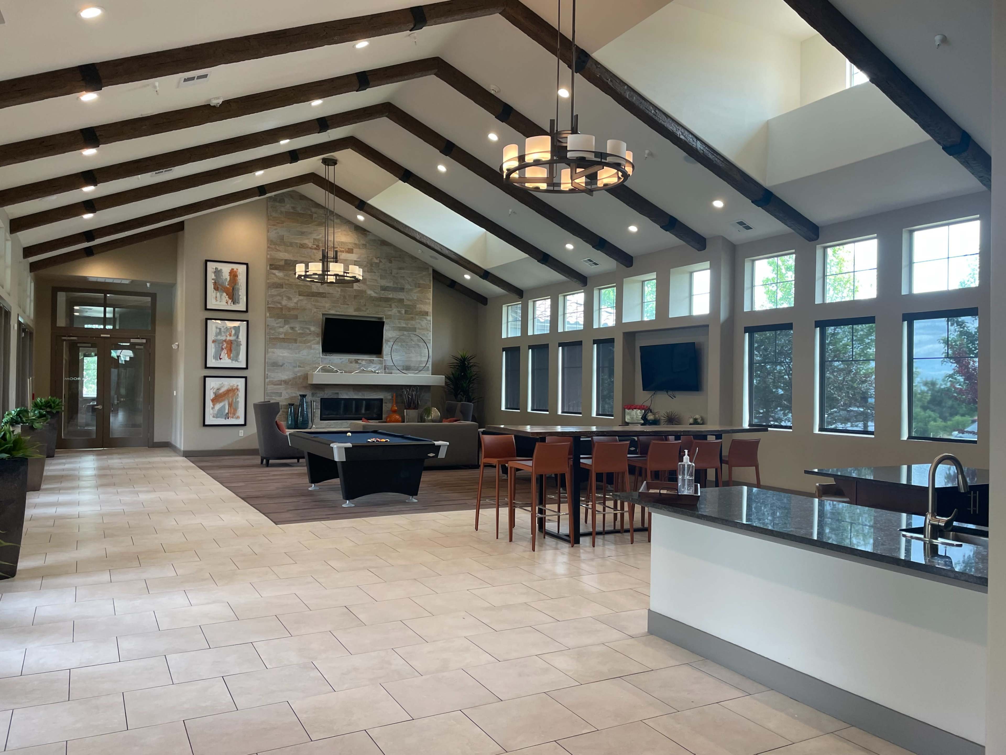 The image shows a spacious modern interior with high vaulted ceilings, featuring a living area with a fireplace, a dining area, and a pool table.