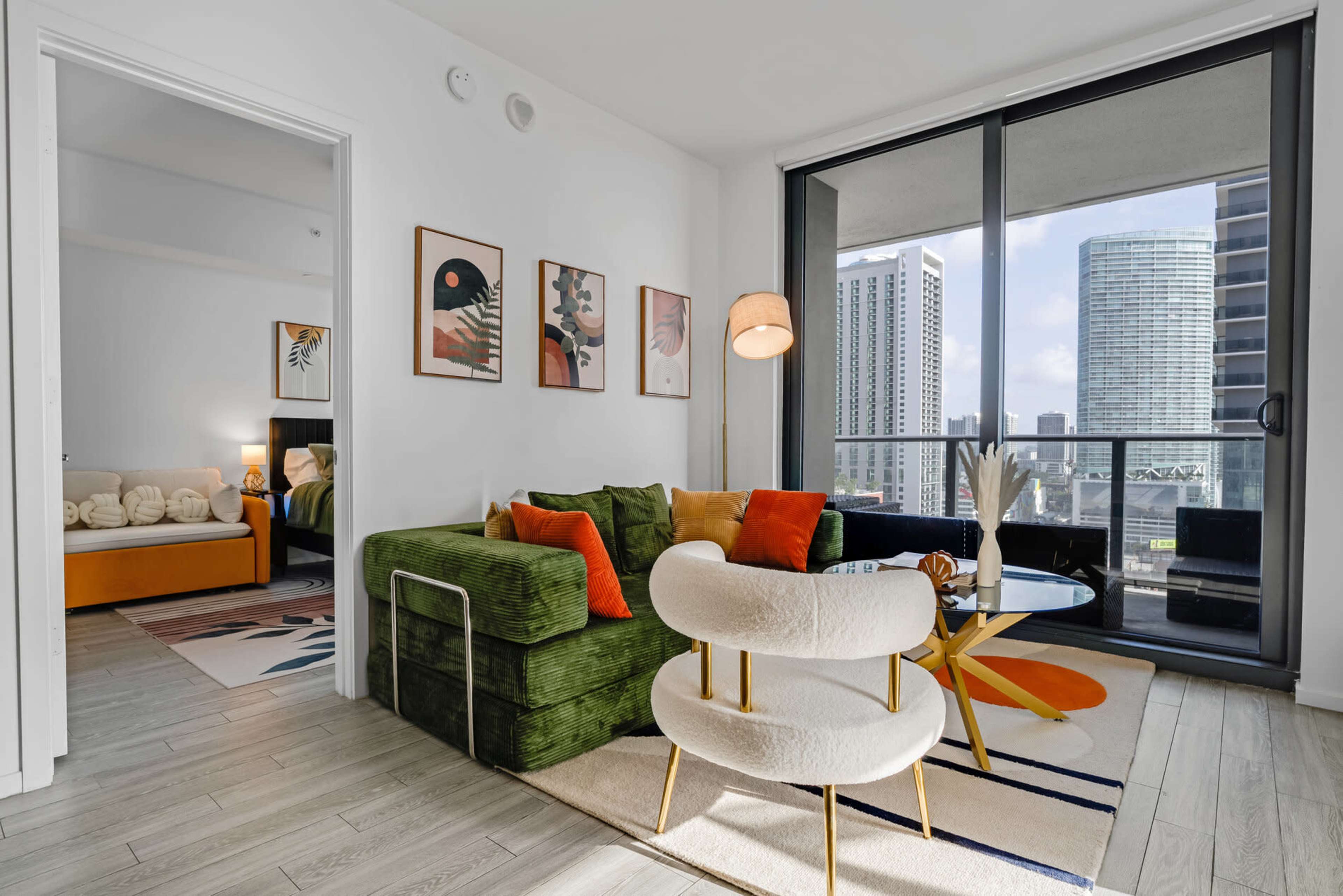 The image shows a modern living room with a green sectional couch, a white chair, and large windows overlooking a city skyline.